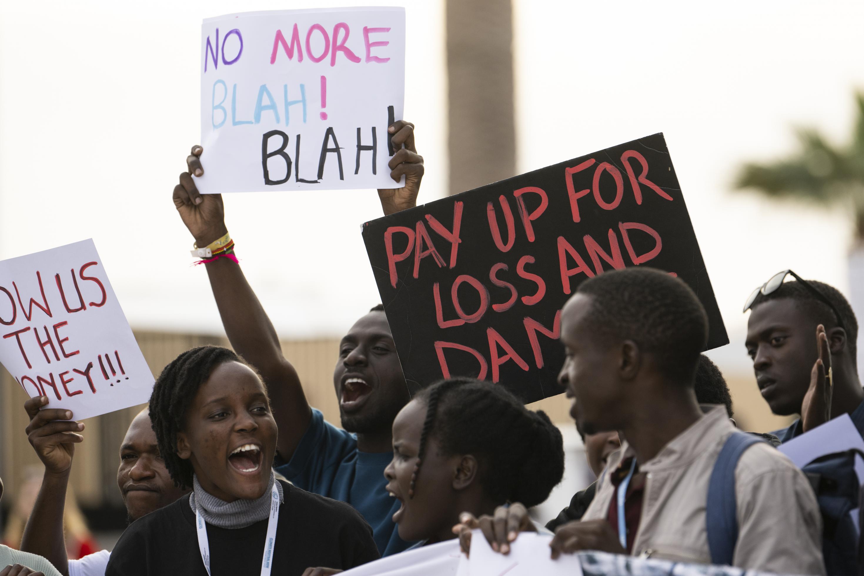 Demonstrierende halten Plakate hoch mit der Aufschrift, in der Übersetzung: „Kein Blabla mehr“ und „Zahlt für Schäden und Verluste“.