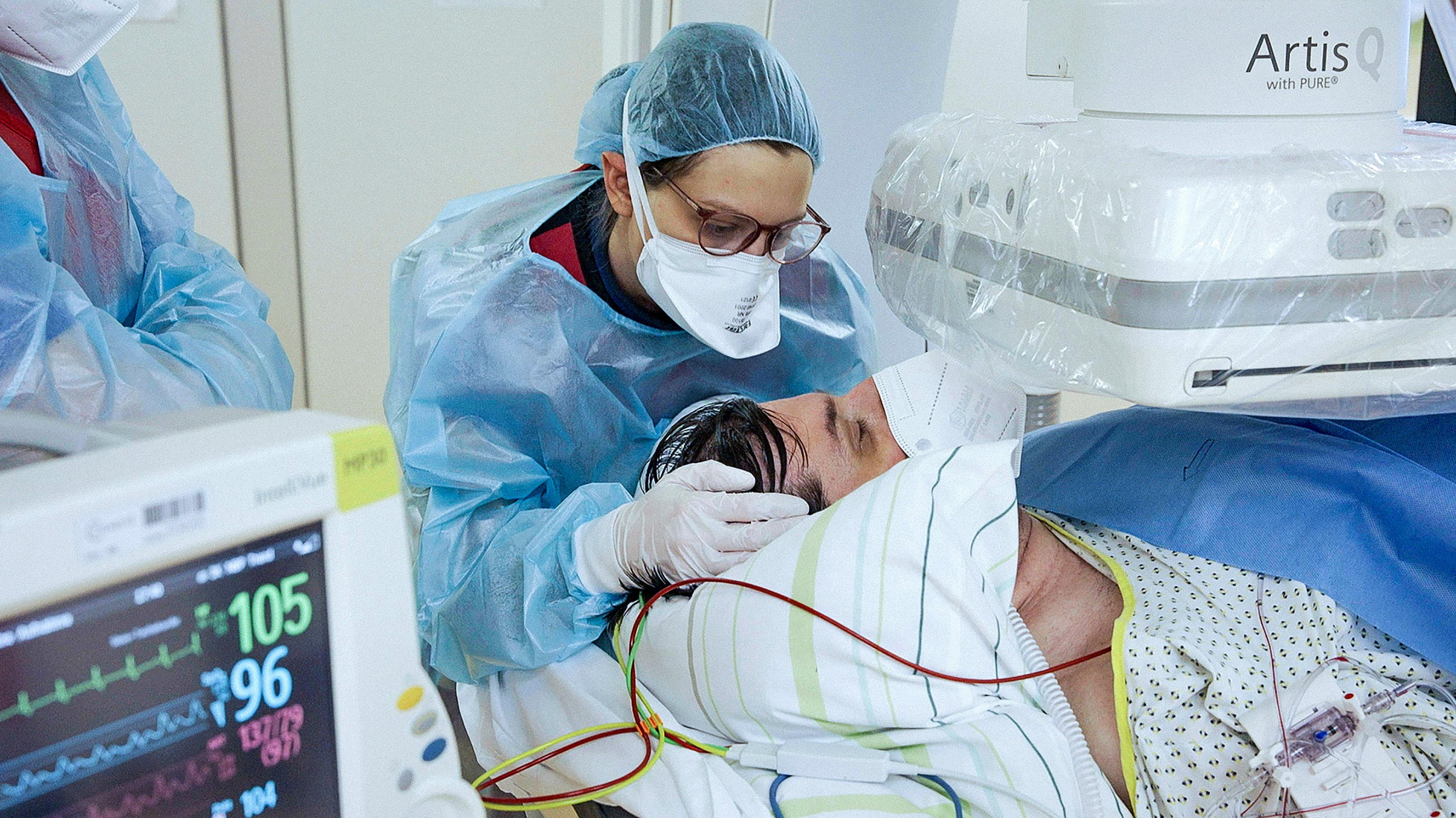 Intensivmedizinerin Sarah Kamel in Schutzkleidung und mit Schutzmaske bei einem Patiententransport, sie hält dabei den Kopf eines Patienten.