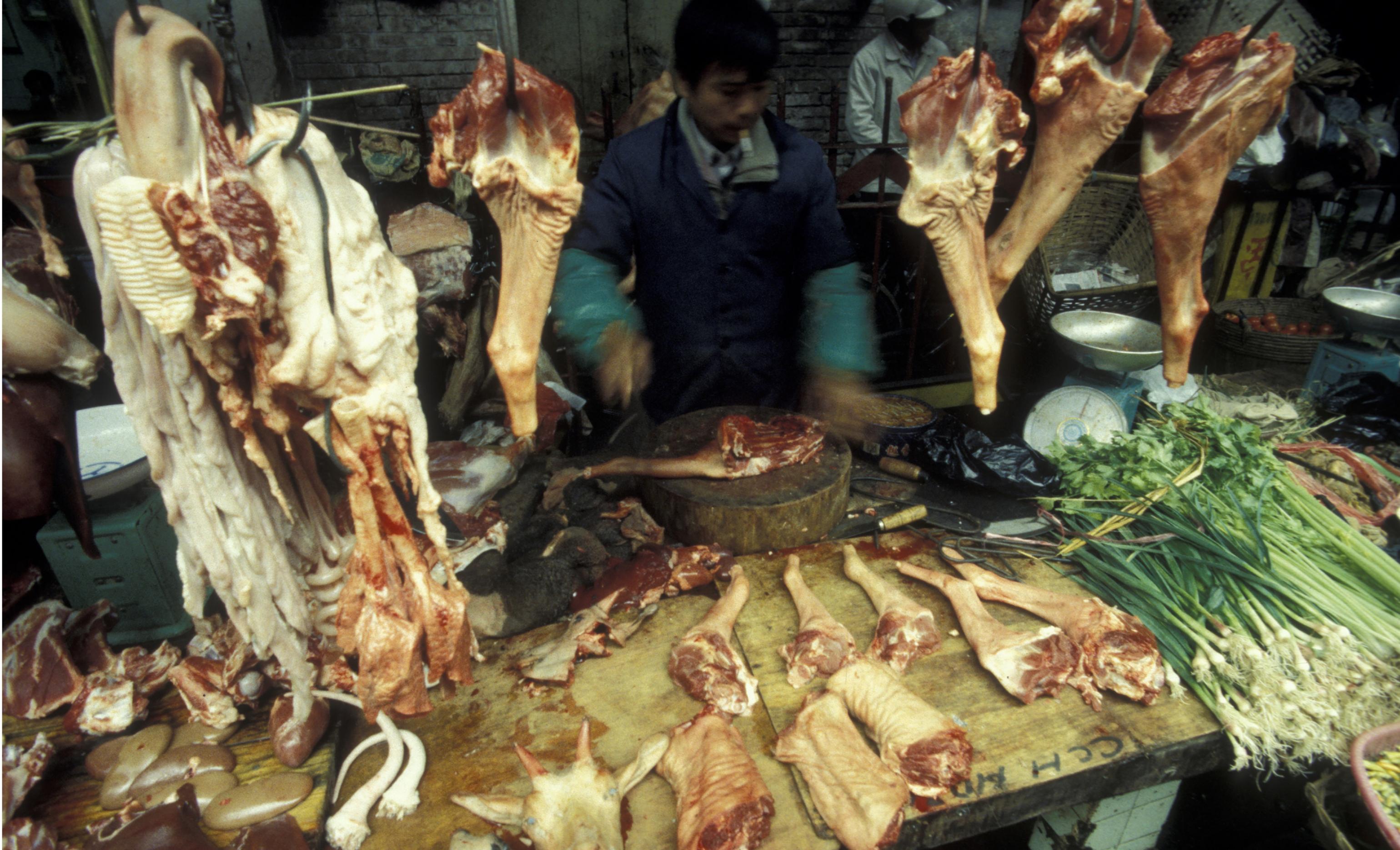 Ein Händler steht hinter seiner Theke auf dem  Fleischmarkt in der  Stadt Guangzhou. Vor ihm liegen viele Fleischstücke.