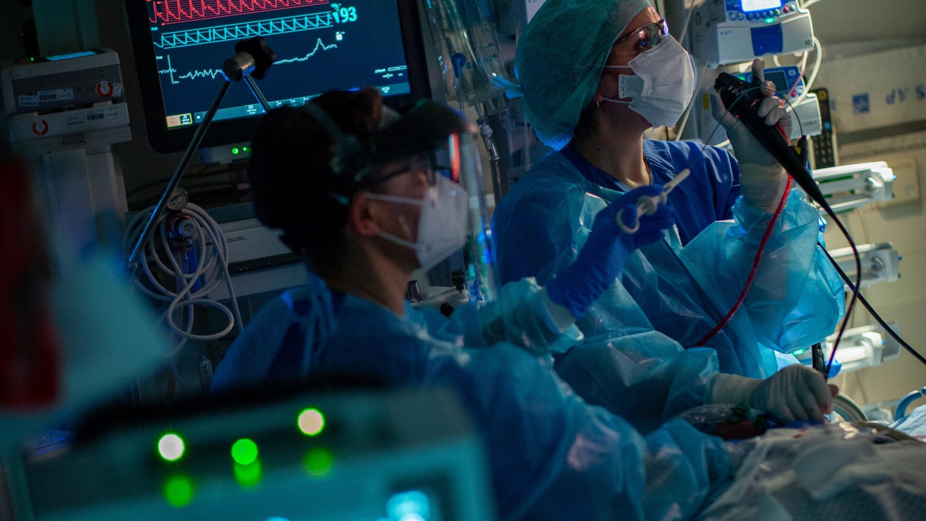 Intensivstation mit Bildschirmen. Zwei Mediziner in Schutzkleidung versorgen einen Covid-Patienten.