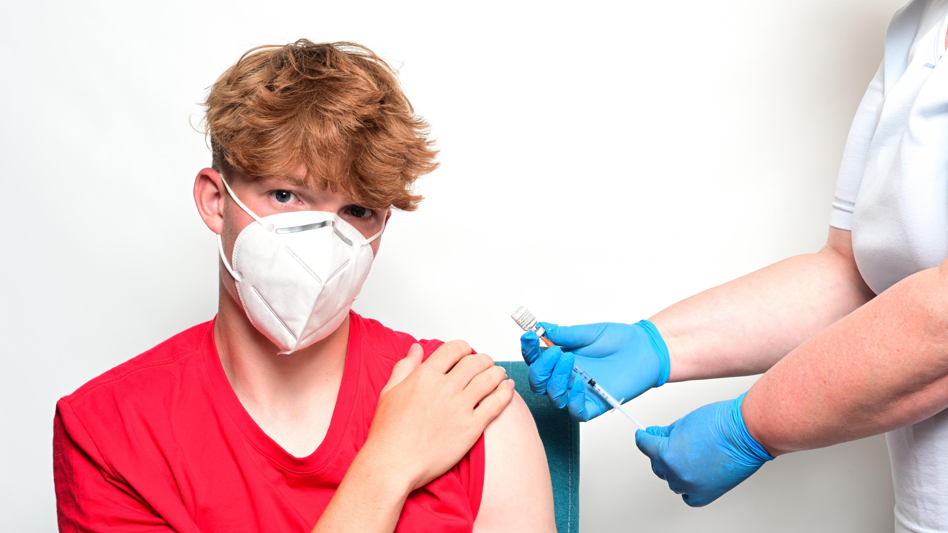 Ein Jugendlicher im roten T-Shirt wird mit dem Impfstoff Comirnaty von BioNTech/Pfizer in den linken Oberarm geimpft.