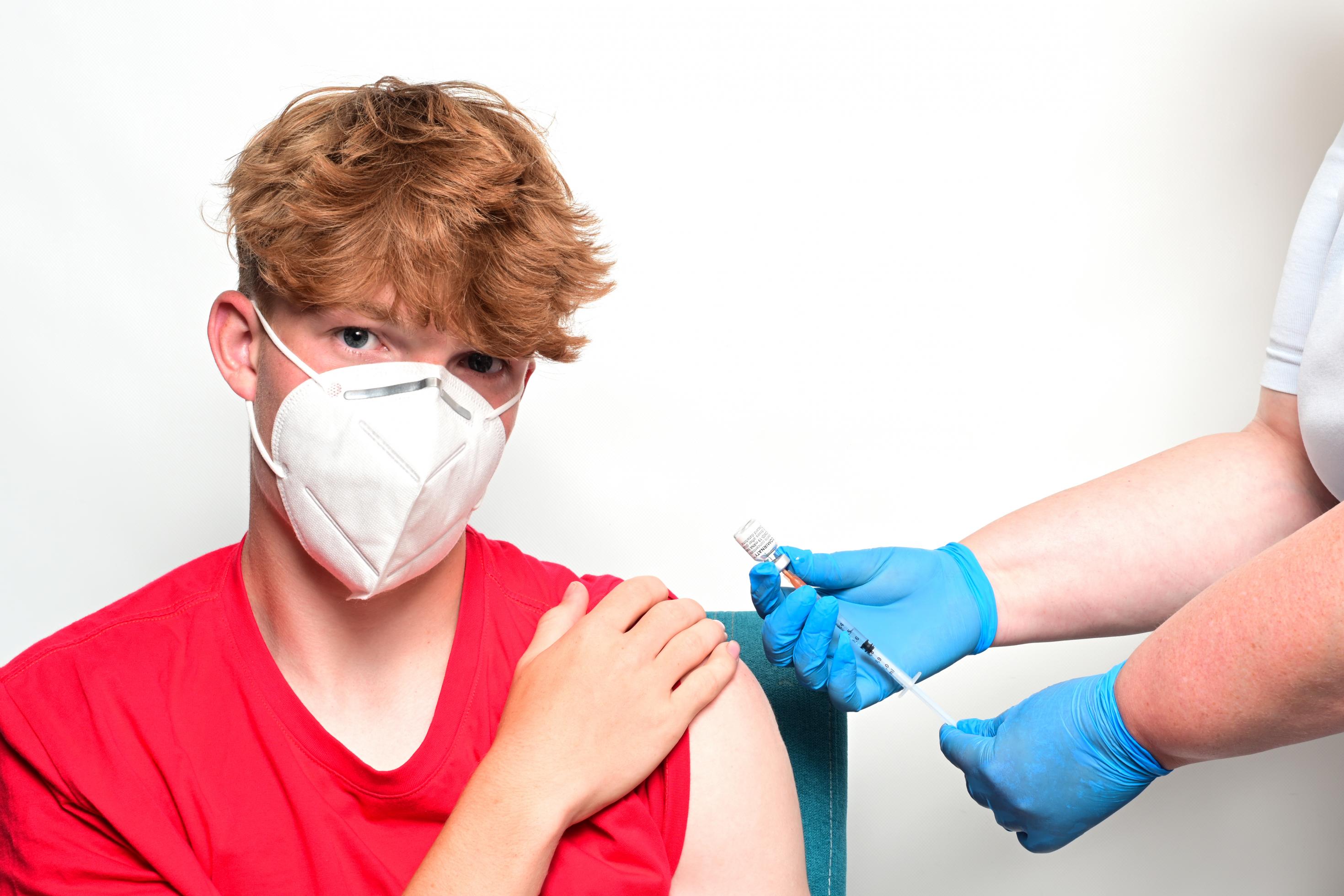 Ein Jugendlicher im roten T-Shirt wird mit dem Impfstoff Comirnaty von BioNTech/Pfizer in den linken Oberarm geimpft.