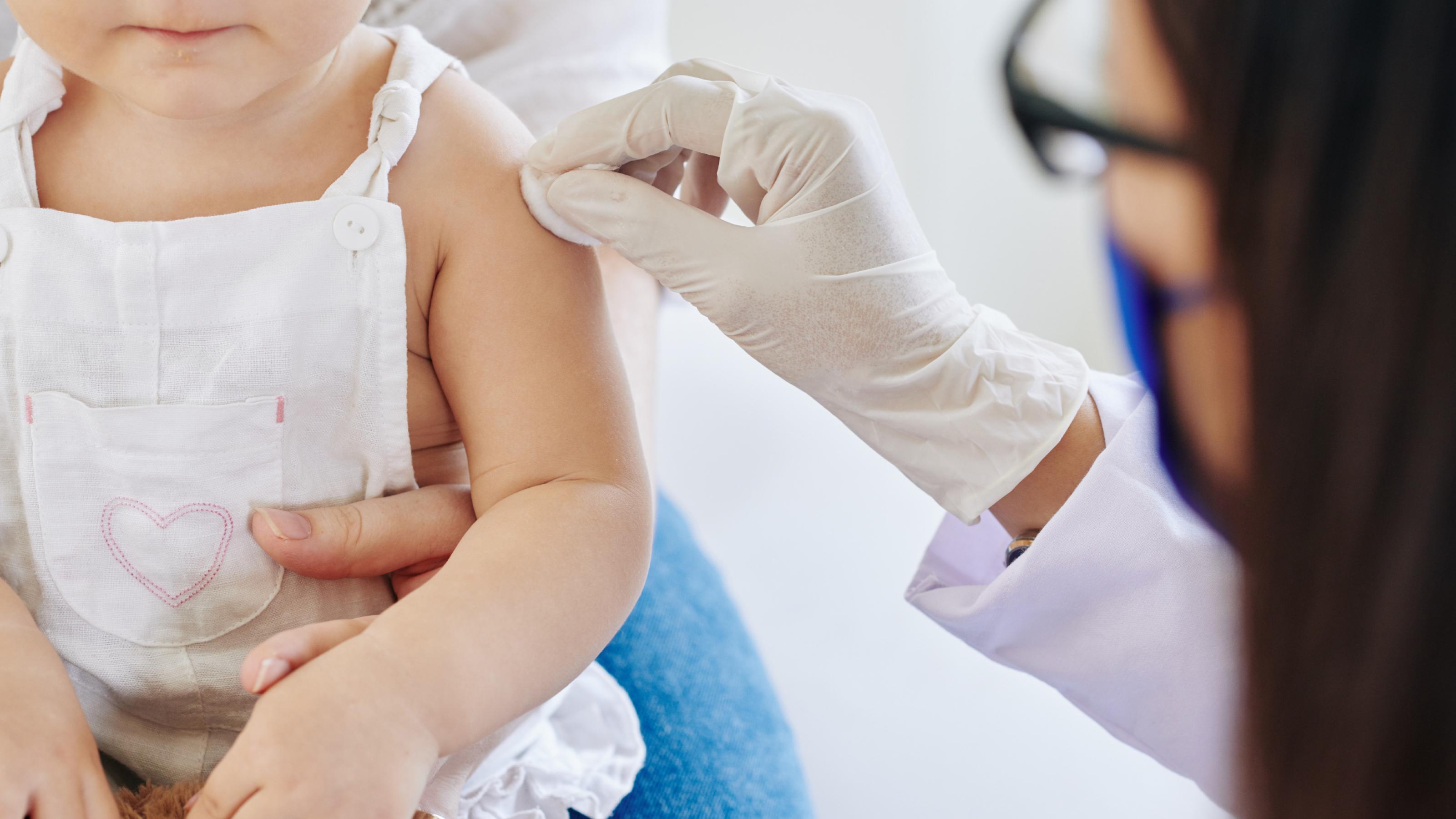 Eine Ärztin desinfiziert vor der Impfung den Arm eines Kleinkinds.