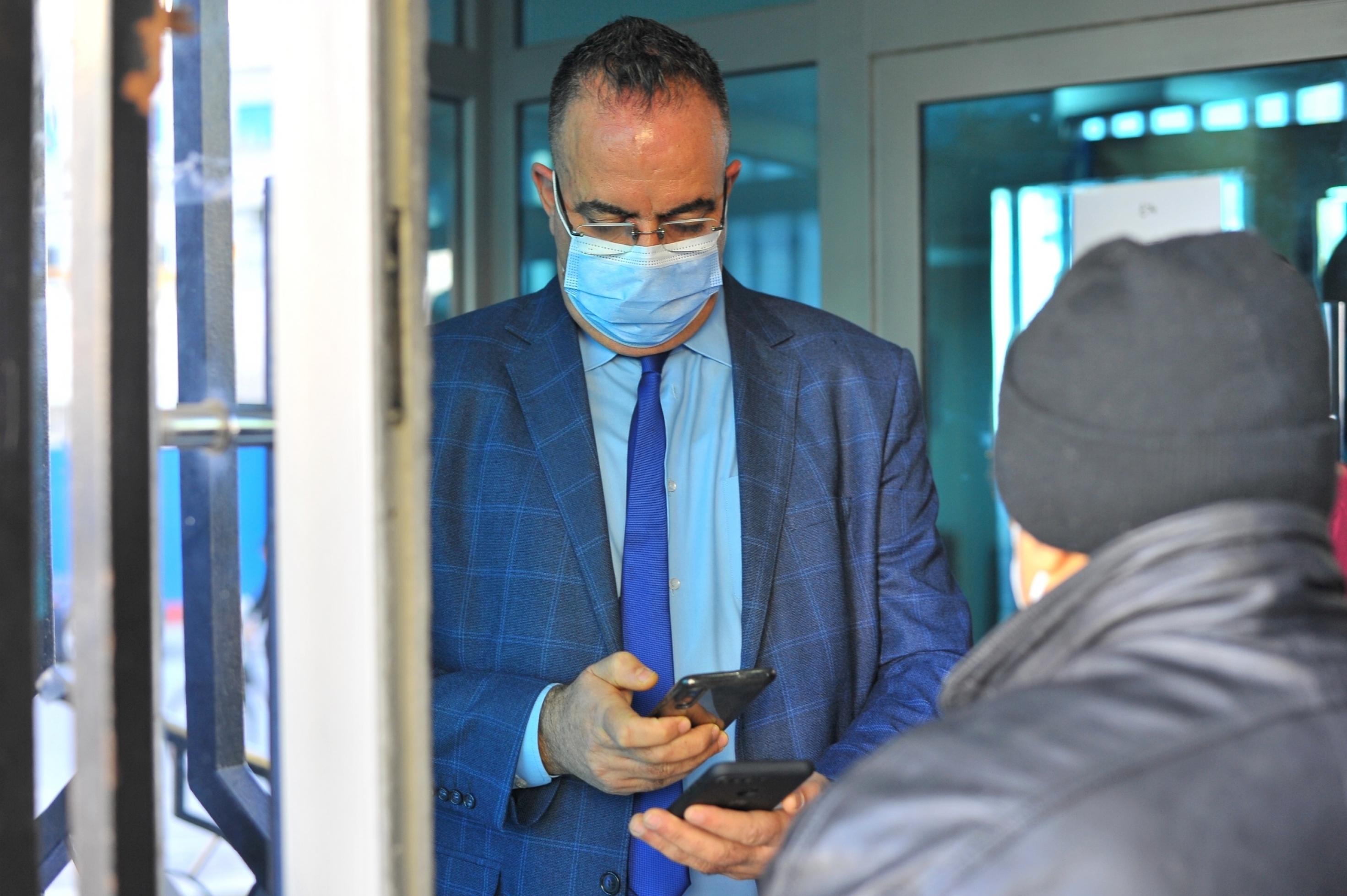 Ein Angestellter mit Anzug und Krawatte am Eingang eines offiziellen Gebäudes in Tunies kontrolliert den Impfnachweis eines Besuchers.