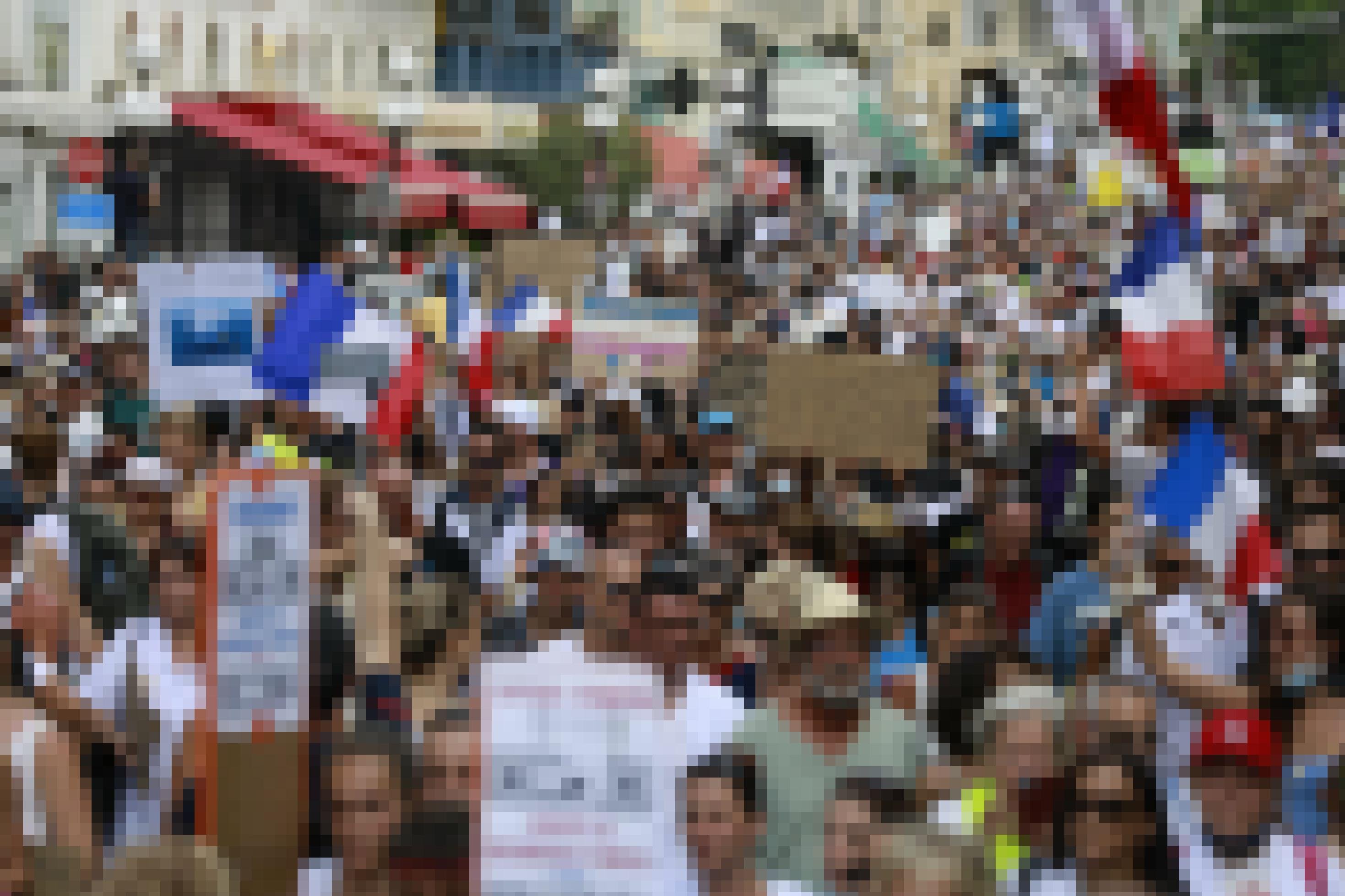 Eine Menschenmenge weitgehend ohne Maske bewegt sich durch die Straße, mit vielen handgemalten Plakaten