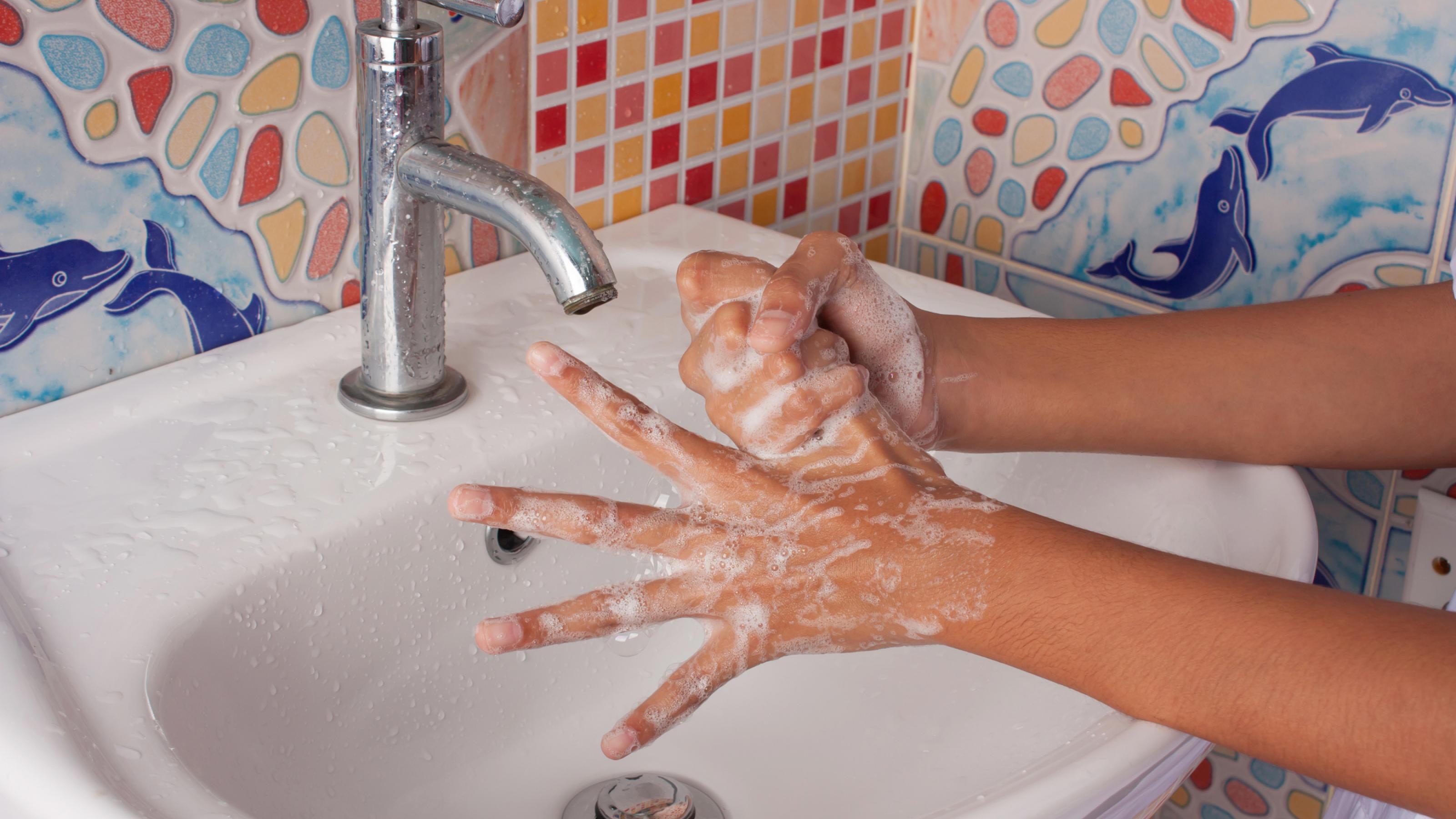 Das Bild zeigt die Hände eines Mädchens, das diese mit Seife in einem Waschbecken wäscht.