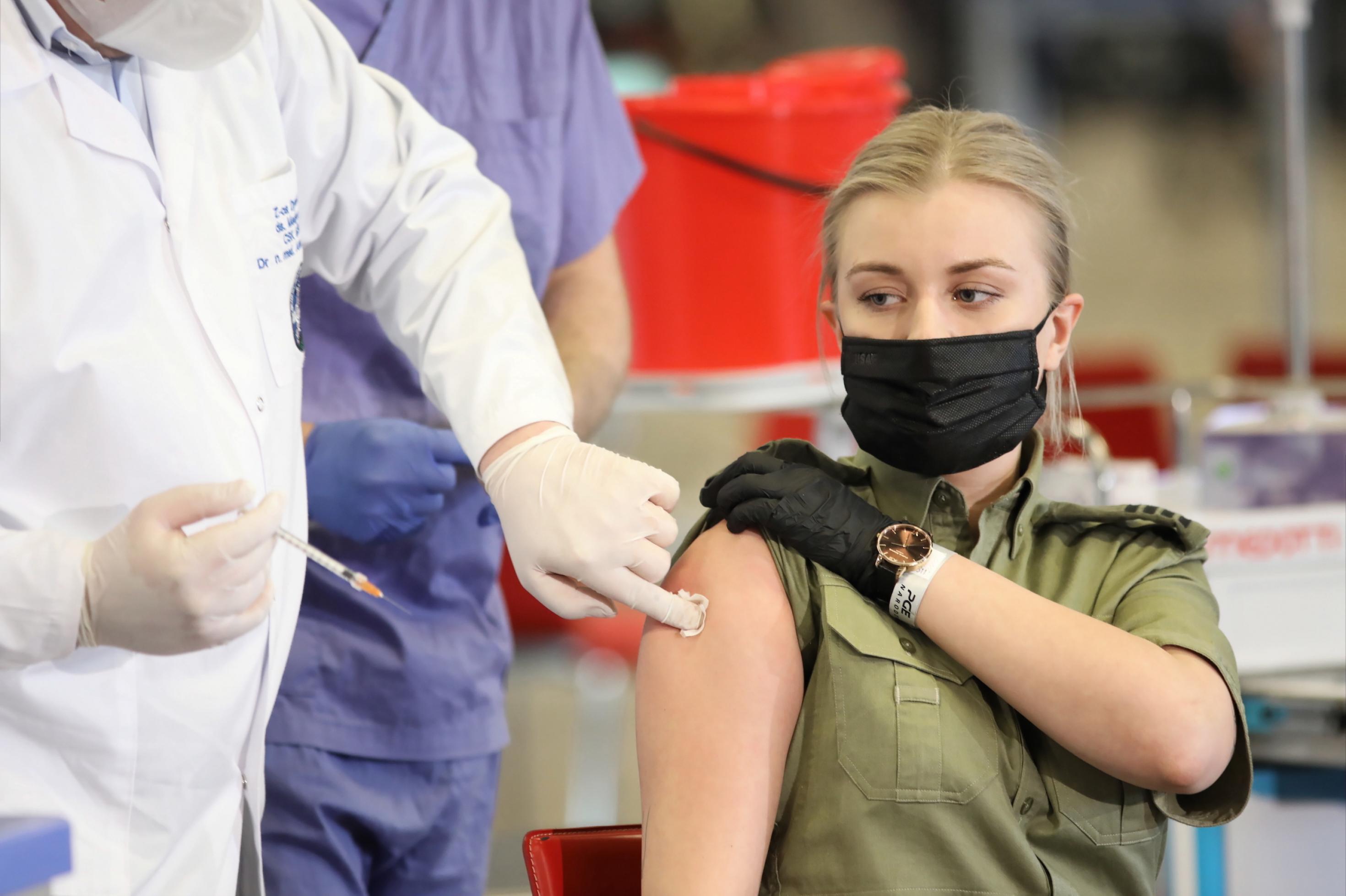 Eine junge blonde Soldatin sitzt auf einem Stuhl und bekommt den Astra-Zeneca-Impfstoff.