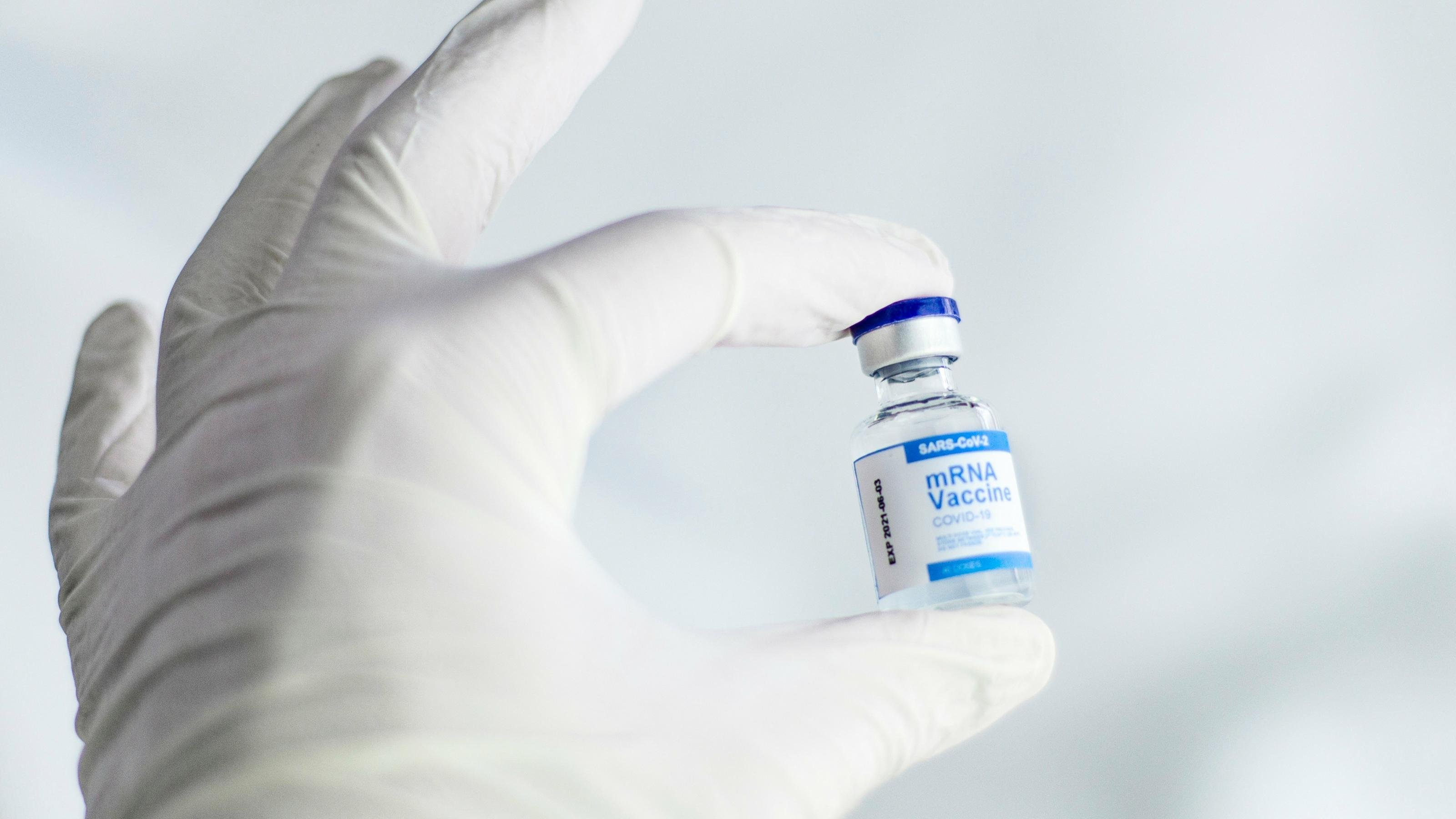 Im Labor hält eine Hand mit einem Einmalhandschuh ein Glasflaschen mit MRNA-Impfstoff gegen Corona-Viren in die Kamera.