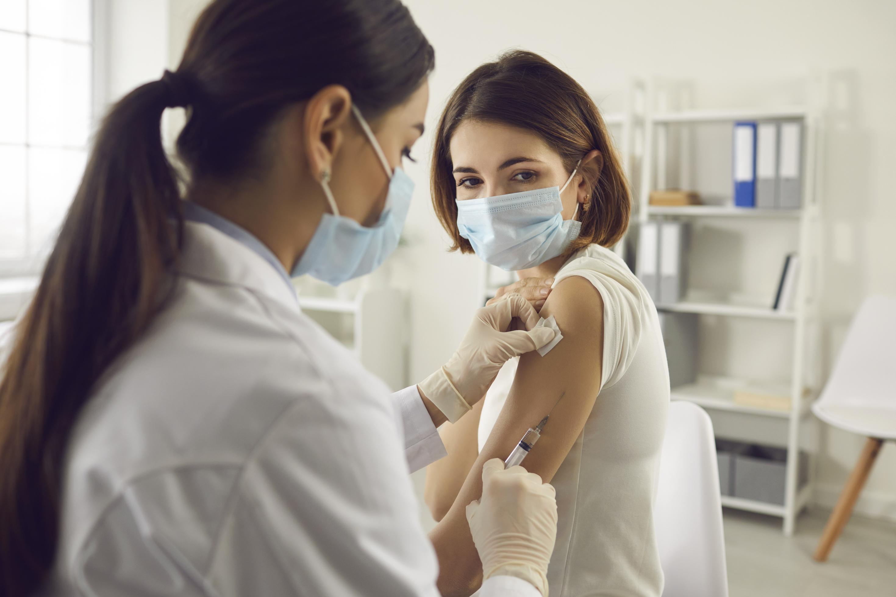 Impfung und Prävention vor Covid-19: Eine Frau mit medizinischer Gesichtsmaske erhält von einer Ärztin eine Impfung gegen Covid-19.