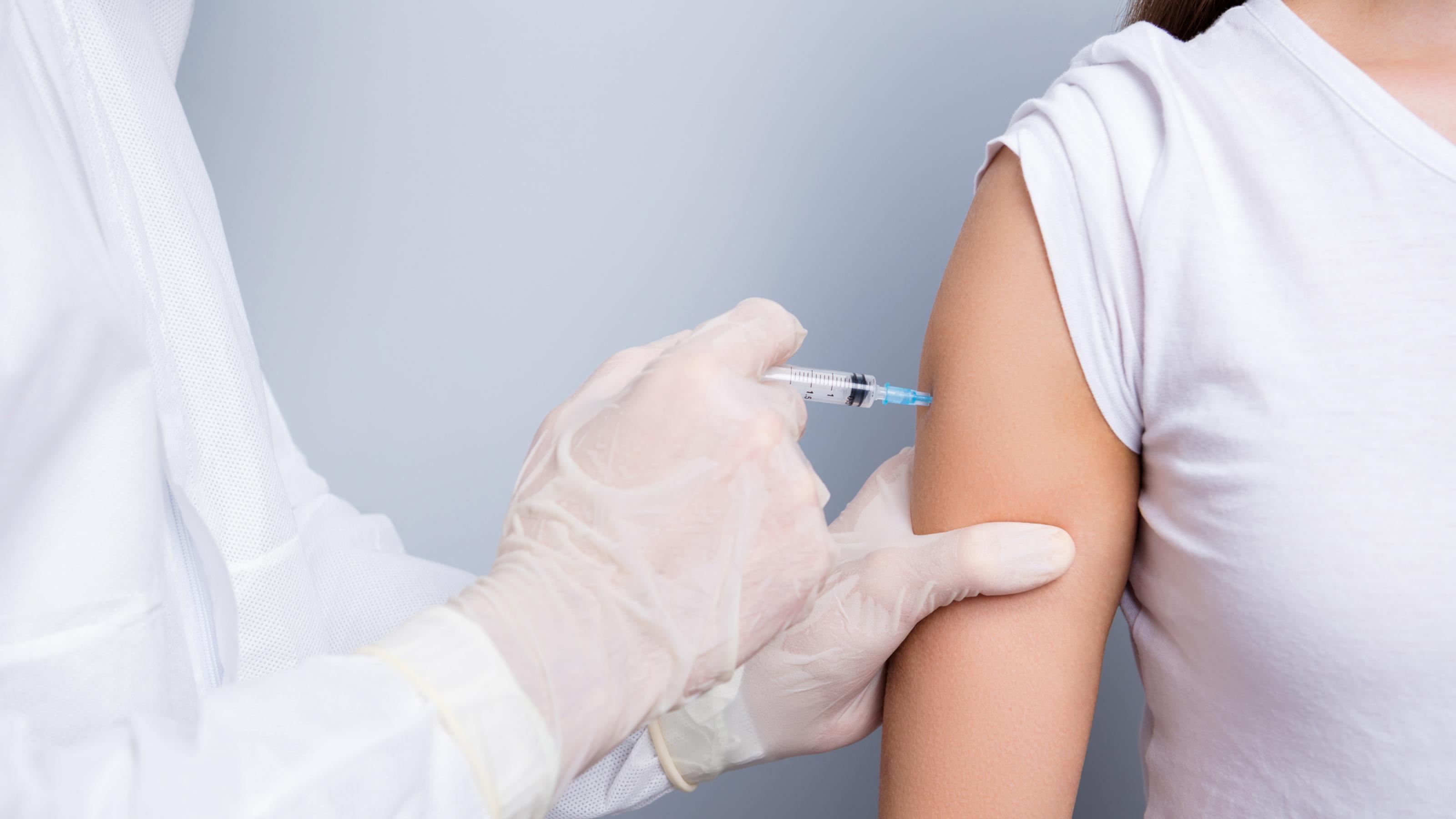 Nahaufnahme einer COVID-19-Impfung: Der Bildausschnitt zeigt den Oberarm einer Frau und die Hand einer Ärztin oder eines Arztes beim Verabreichen der Impf-Spritze.