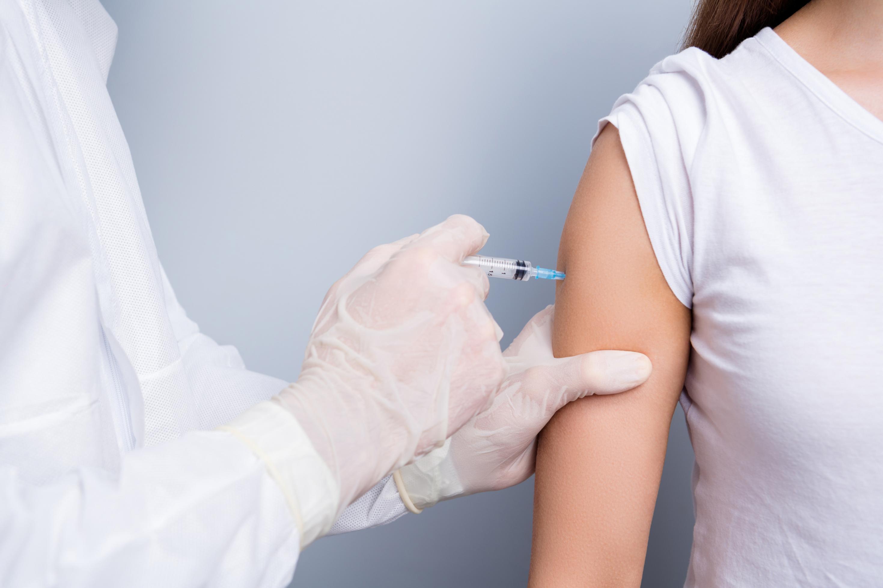 Nahaufnahme einer COVID-19-Impfung: Der Bildausschnitt zeigt den Oberarm einer Frau und die Hand einer Ärztin oder eines Arztes beim Verabreichen der Impf-Spritze.
