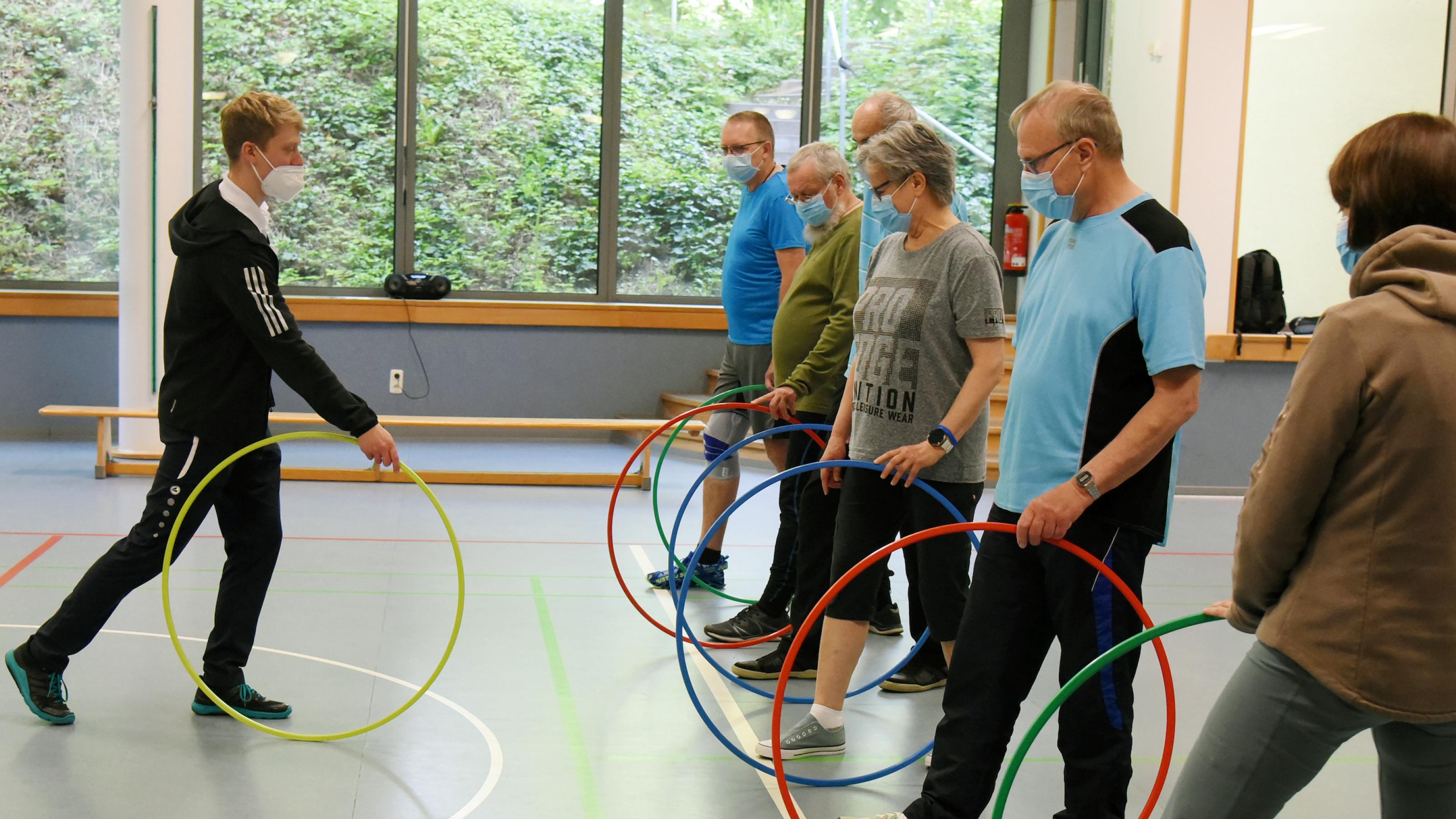 Reha-Therapie, der Trainer zeigt einer Gruppe mittelalter Menschen Bewegungsabläufe mit einem Gymnastikreifen