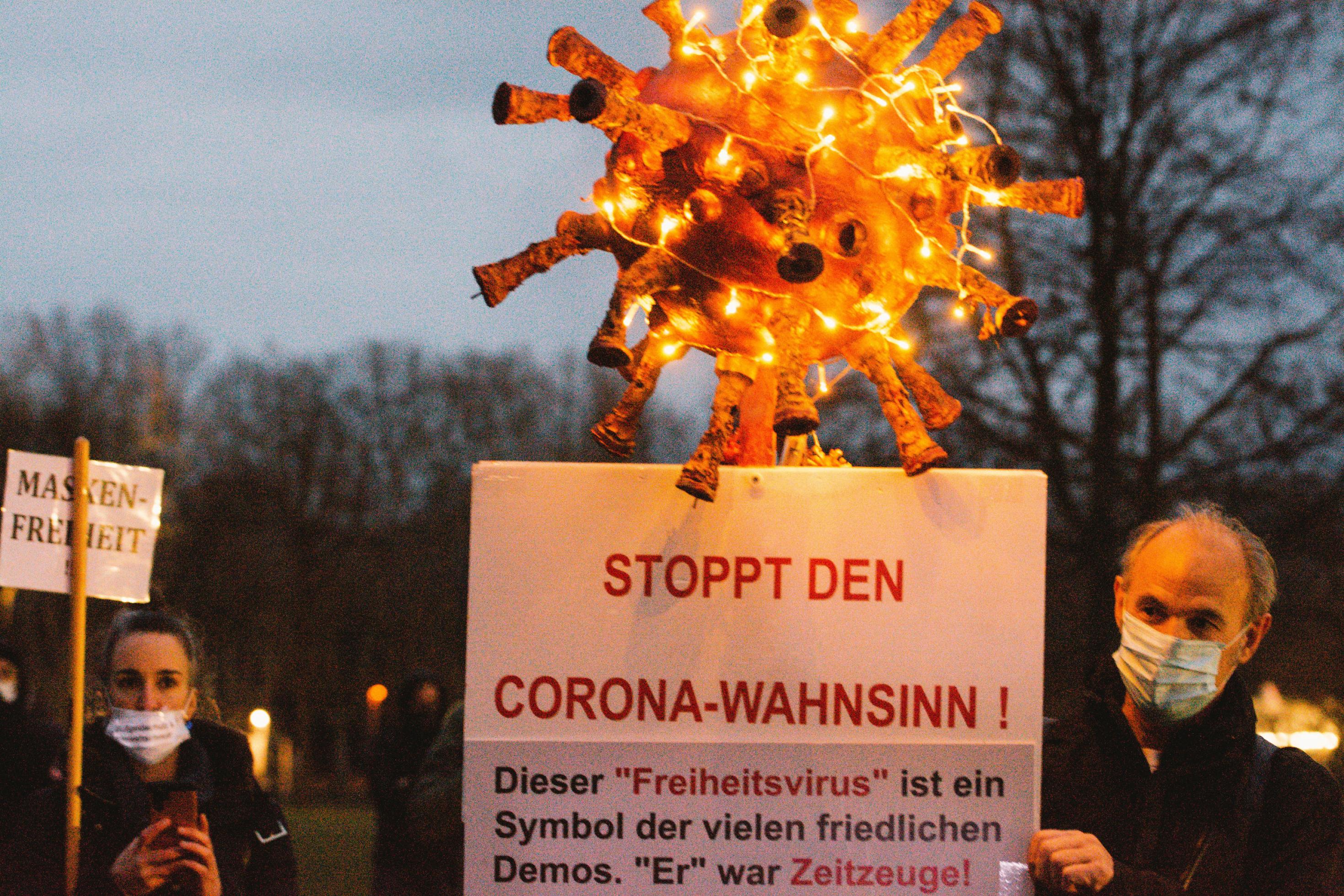 Mann hält auf Demo ein beleuchtetes Papp-Coronavirus hoch mit Schild, dies sei ein „Freiheitsvirus“