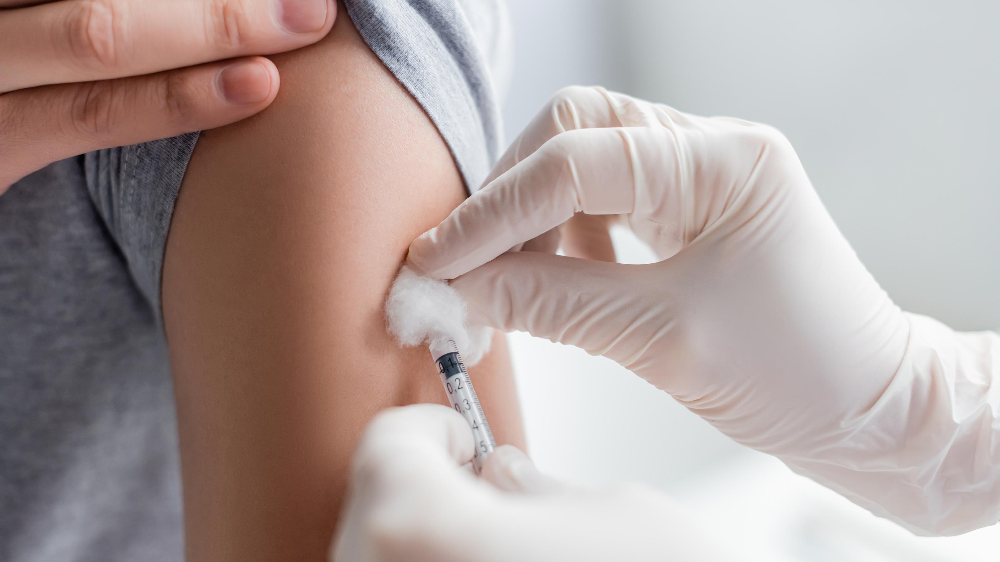 Das Bild zeigt den Oberarm eines jungen Menschen, in den gerade ein Impfstoff injiziert wird.