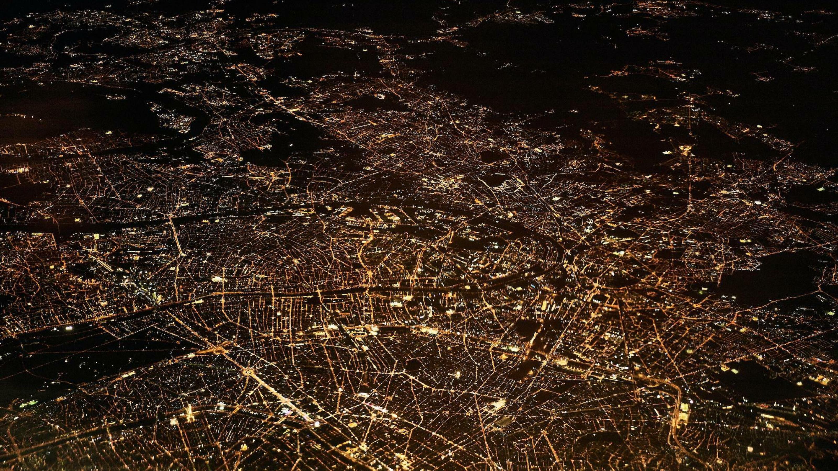 Das Bild zeigt Paris bei Nacht aus der Luft. Zu sehen ist das Netzwerk der beleuchteten Straßen.