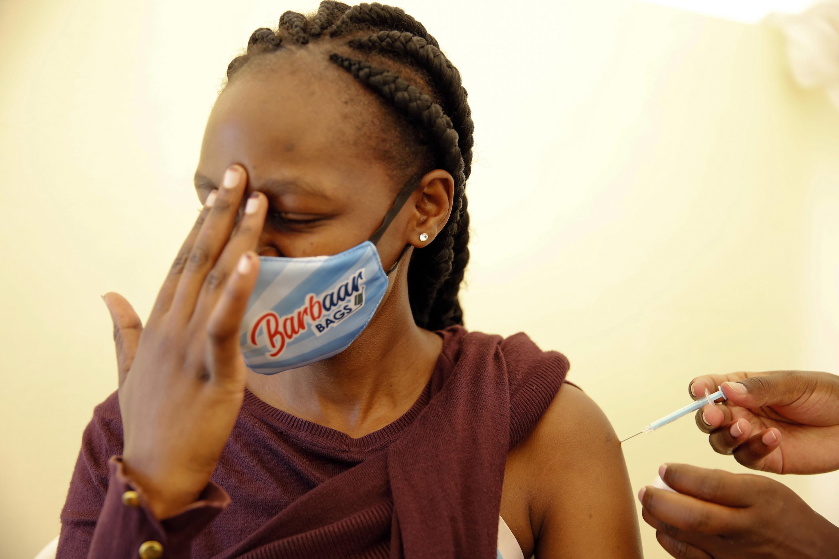 Die junge schwarze Frau hält sich die Finger ihrer rechten Hand an die Stirn, während sie die Impfspritze in den linken Oberarm bekommt.