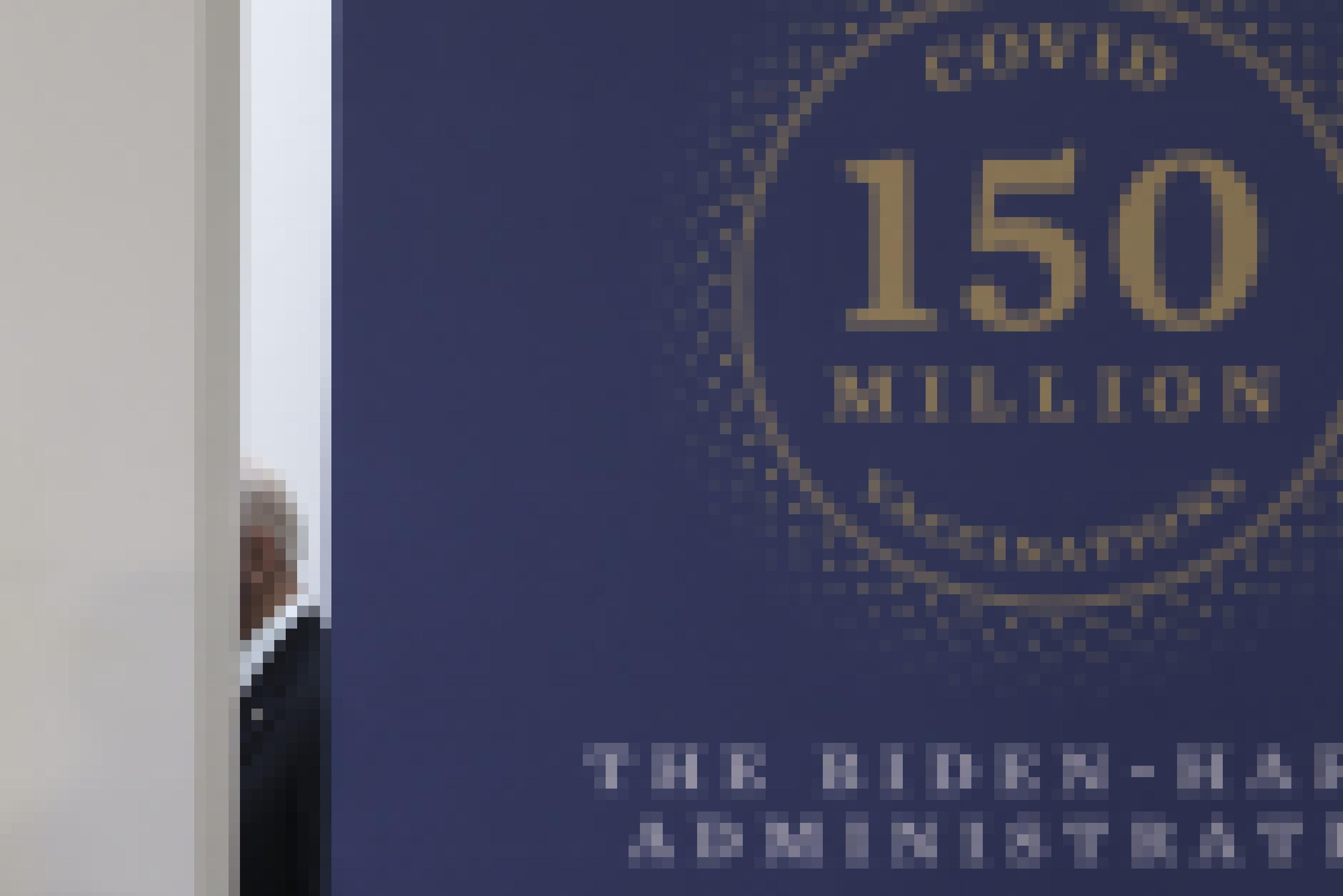 Auf einem großen Schild steht die Zahl von 150 Millionen Impfdosen, dahinter ist in einer Spalte in der Wand US-Präsident Joe Biden zu sehen.