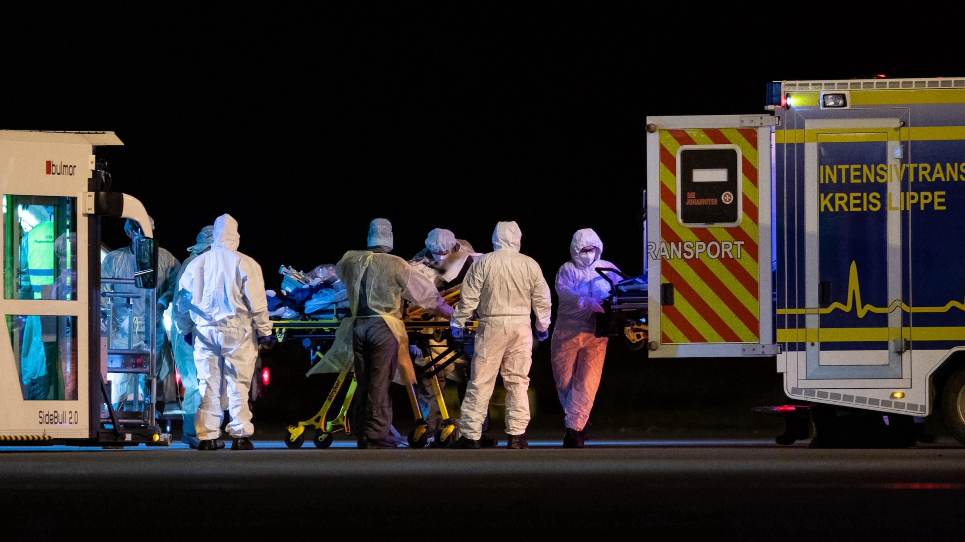 Bei Nacht schieben Fachkräfte einen Kranken auf einer Trage auf einem Flugplatz in einen Krankenwagen.