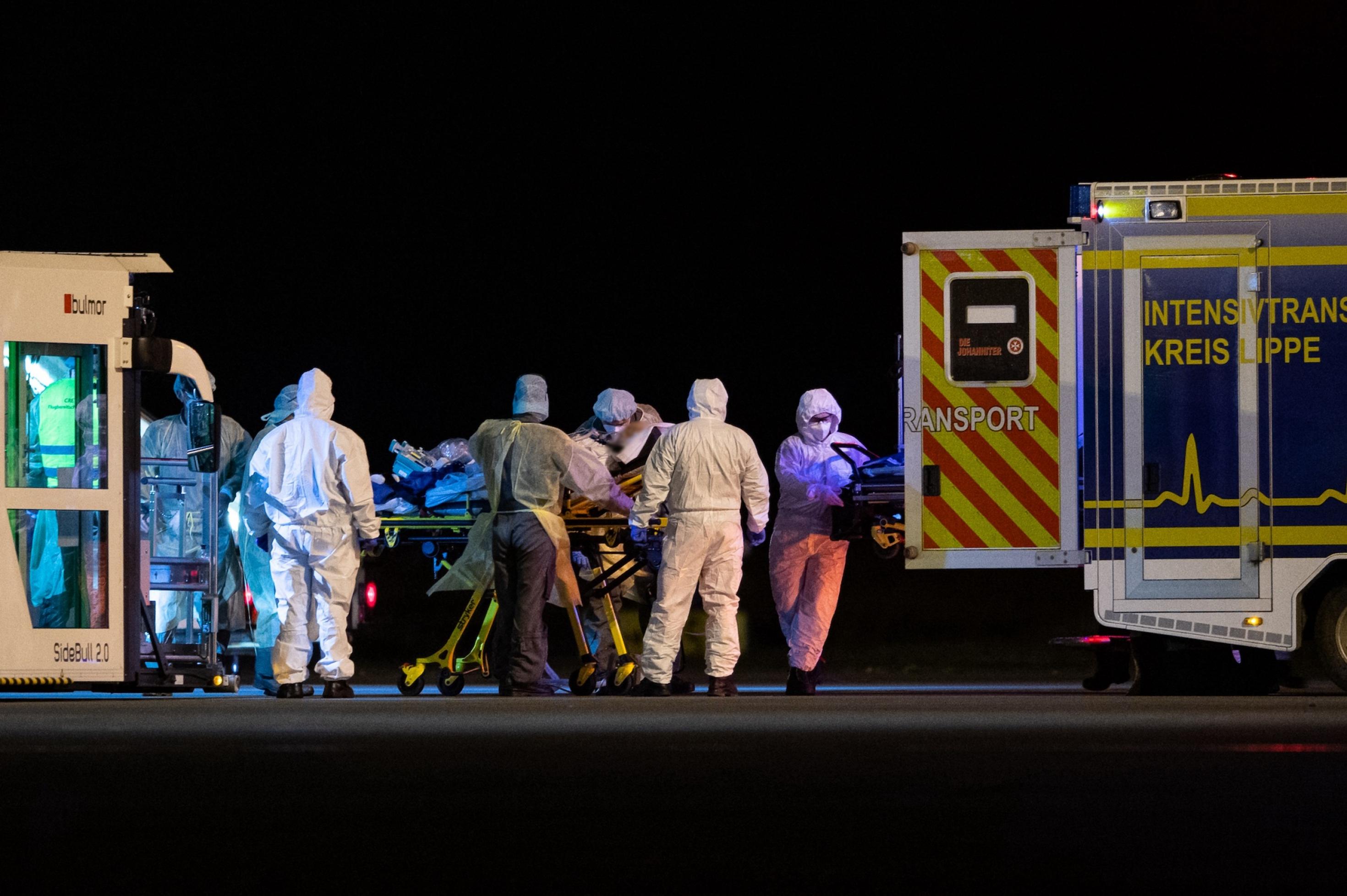 Bei Nacht schieben Fachkräfte einen Kranken auf einer Trage auf einem Flugplatz in einen Krankenwagen.