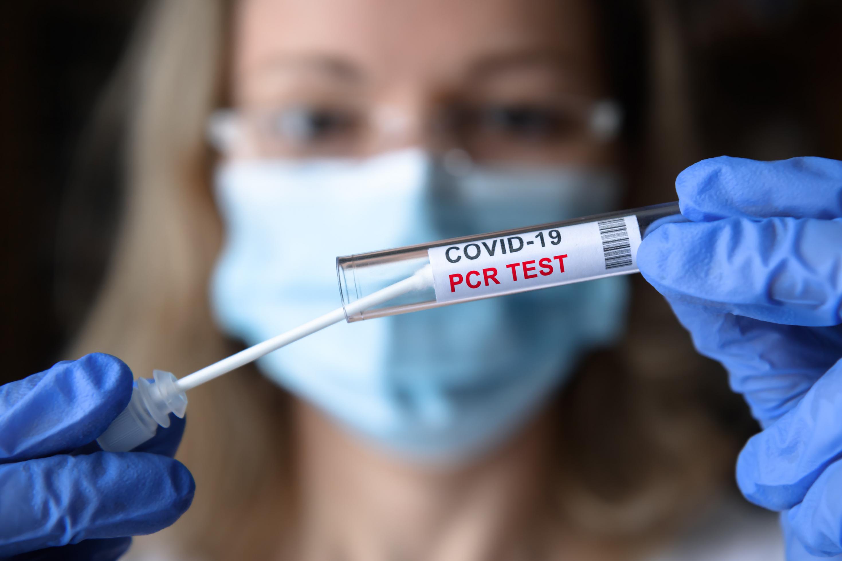 Eine Ärztin hält ein Röhrchen mit einem PCR-Corona-Test vor ihre Augen.