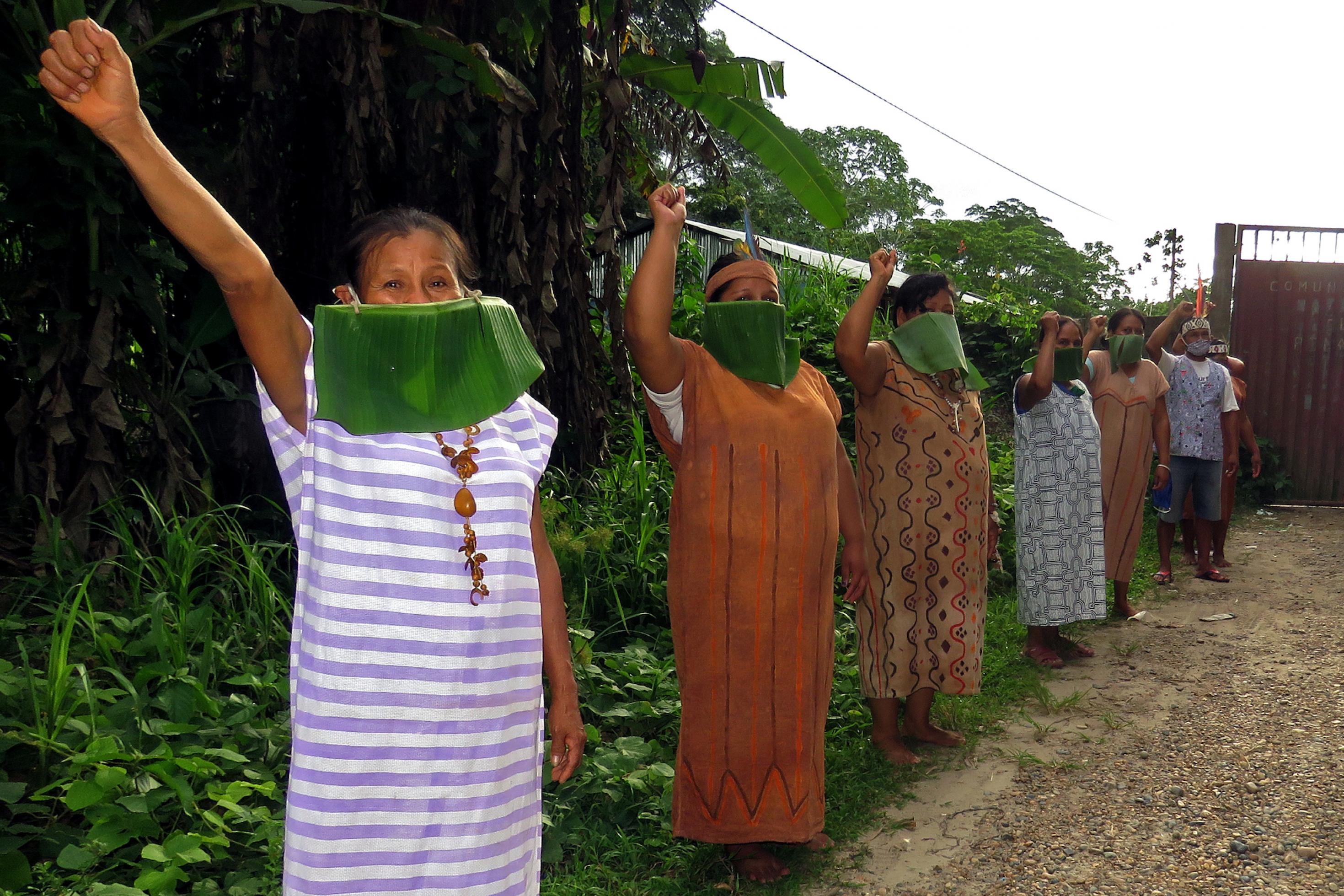 Das Bild zeigt Frauen mit zum Protest ausgestrecktem Arm und geballter Faust. Sie tragen Mundschutz aus Bananenblättern.