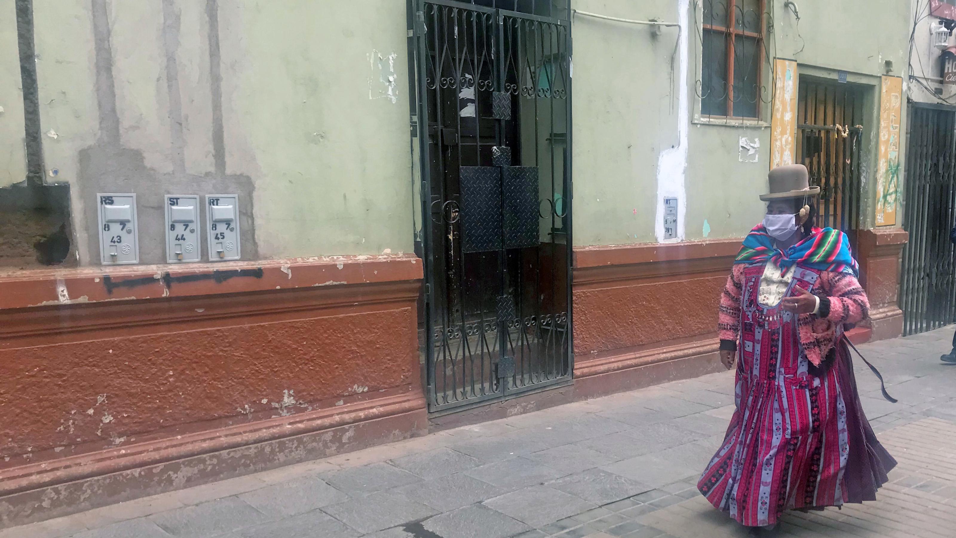 Eine Frau in traditioneller Kleidung geht in Mundschutz auf einer unbelebten Strasse.