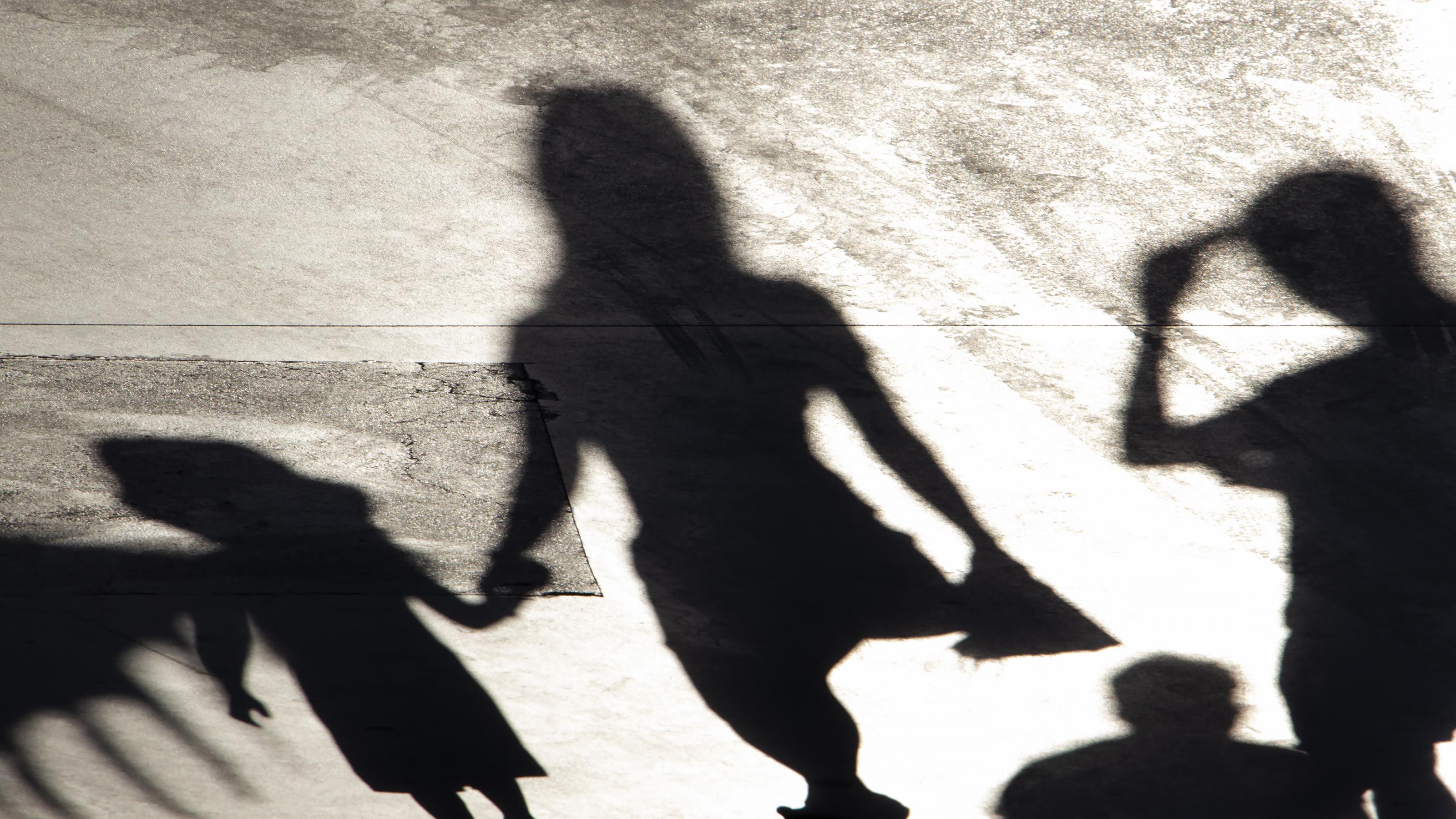 Das Bild zeigt den Schatten einer Frau mit einem Kind an der Hand, andere Menschen stehen am Bildrand. In der Pandemie kümmerten sich vor allem Frauen um die Kinderbetreuung.