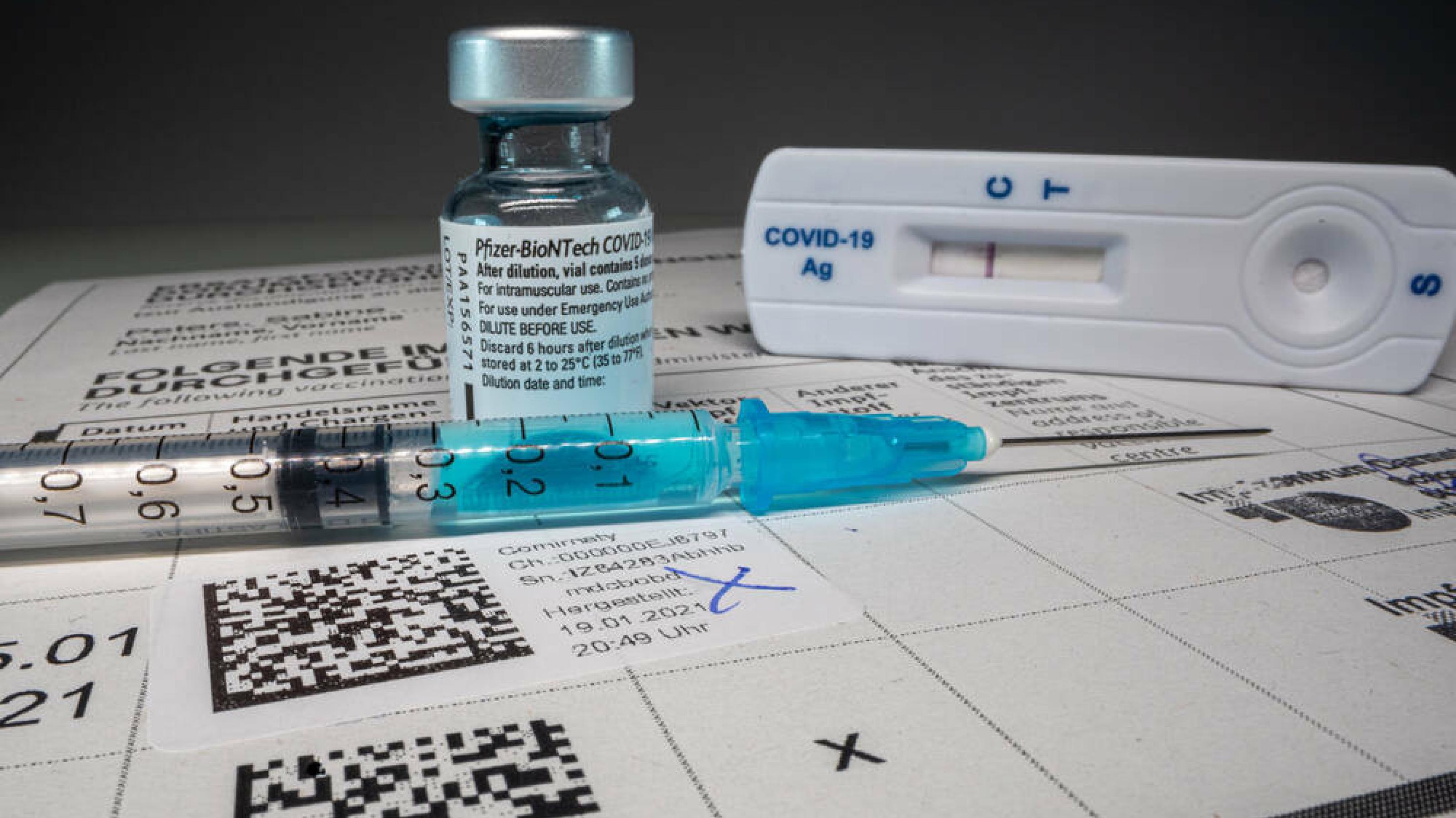 Eine Ampulle Corona-Impfstoff, eine Spritze, ein Schnelltest und ein medizinisches Formular