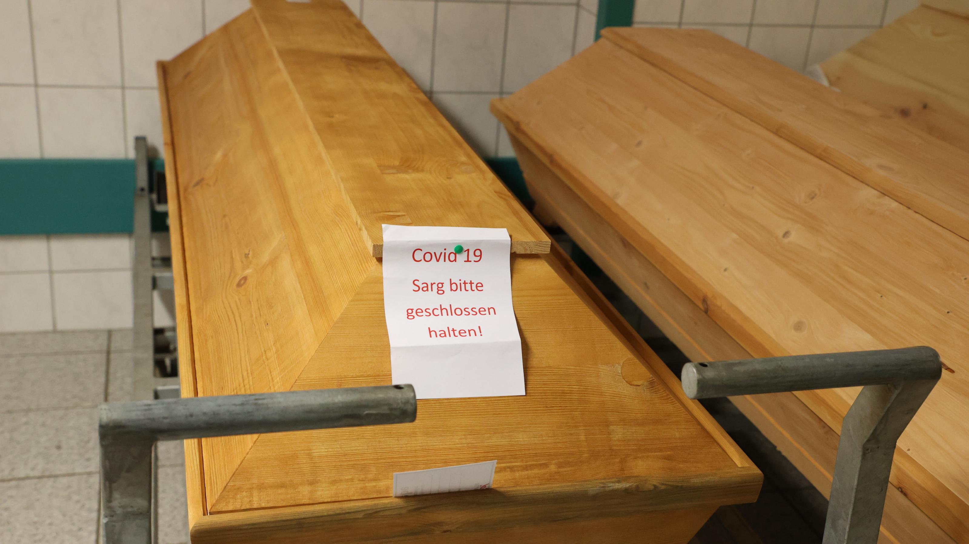 „COVID 19 Sarg bitte geschlossen halten“ steht an einem Sarg im Kühlhaus des städtischen Krematoriums.