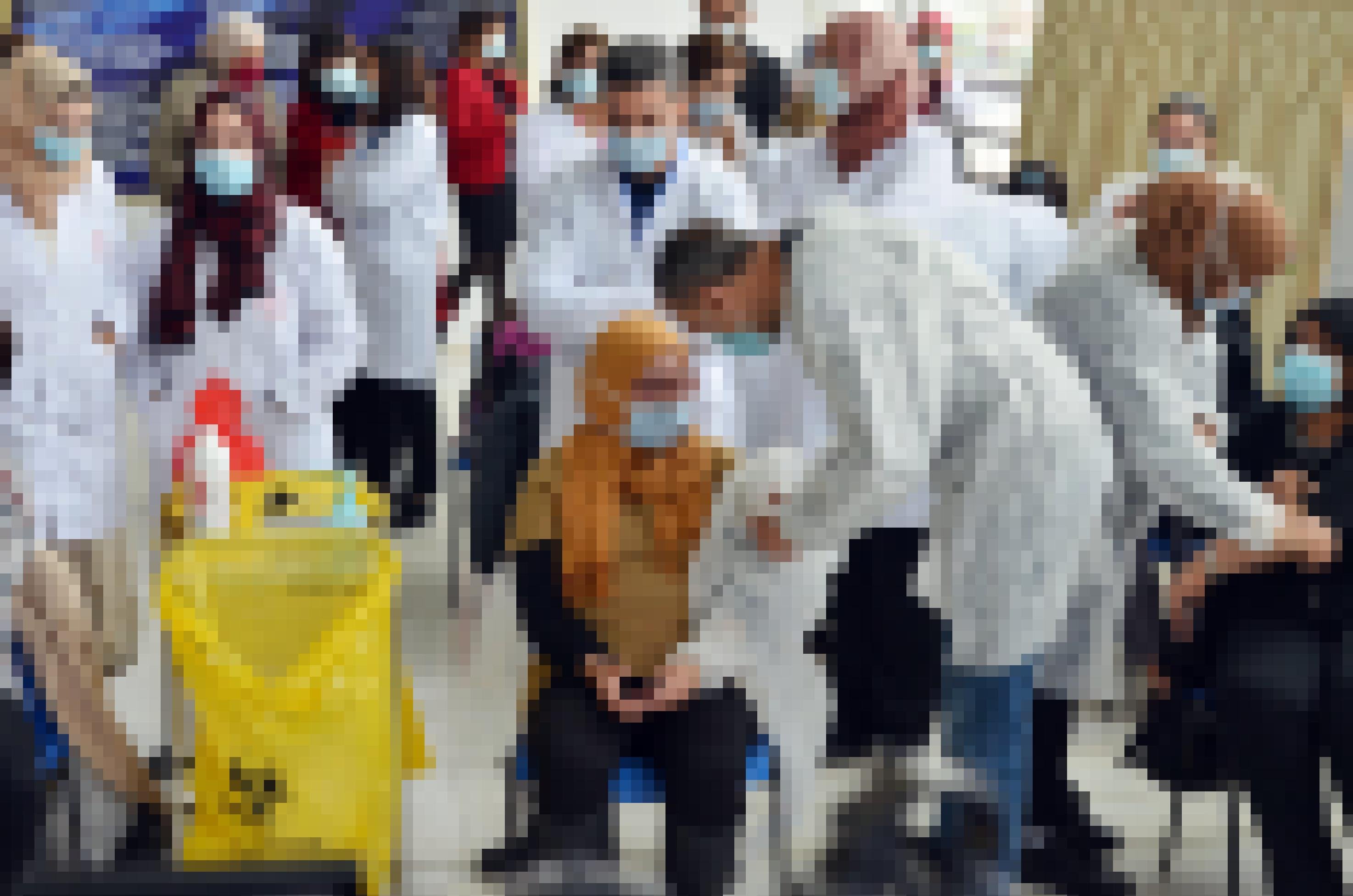 Eine Frau mit Kopftuch bekommt eine Corona-Impfung. Menschen in weißen Kitteln stehen darum.