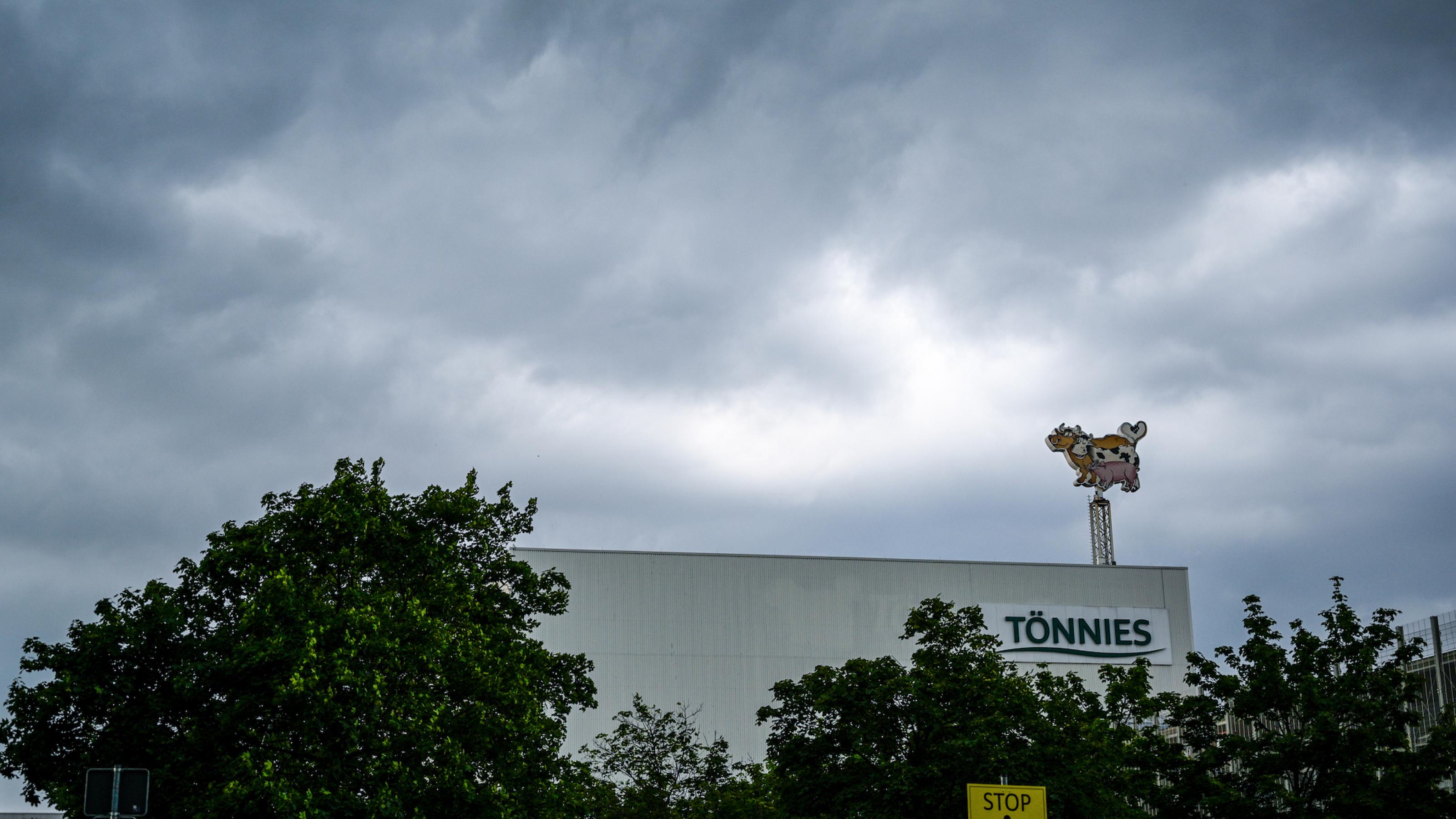 Das Bild zeigt den Firmensitz der Fleischfirma Tönnies im Landkreis Gütersloh, wo es zu einem Massenausbruch des Coronavirus gekommen ist. Auf dem Dach eines Fabrikgebäudes ist eine Leuchtschrift mit einer Kuh und einem Schwein installiert.