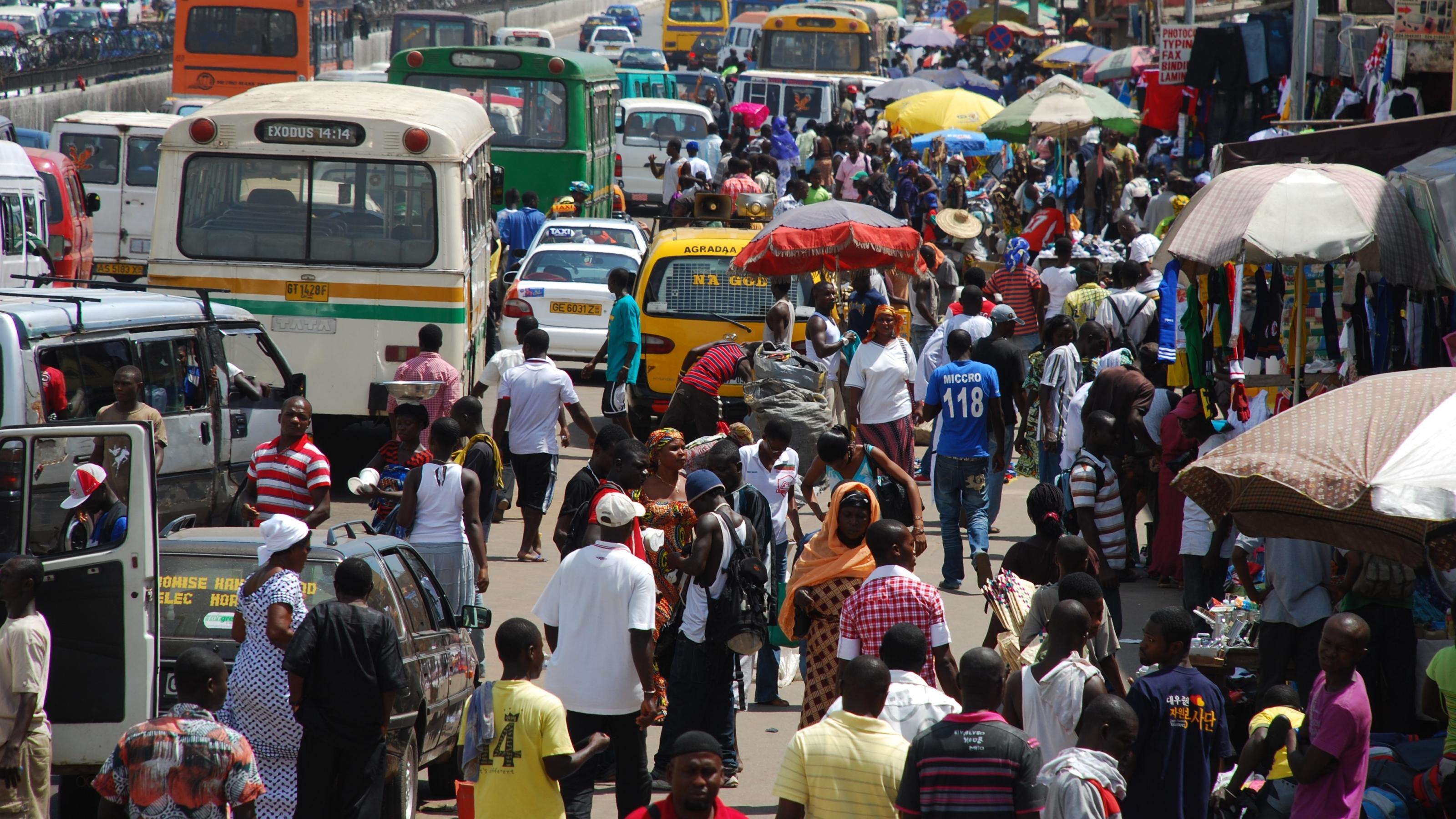 Eine Straße in Ghana. Es sind viele Menschen, Busse und Autos zu sehen.