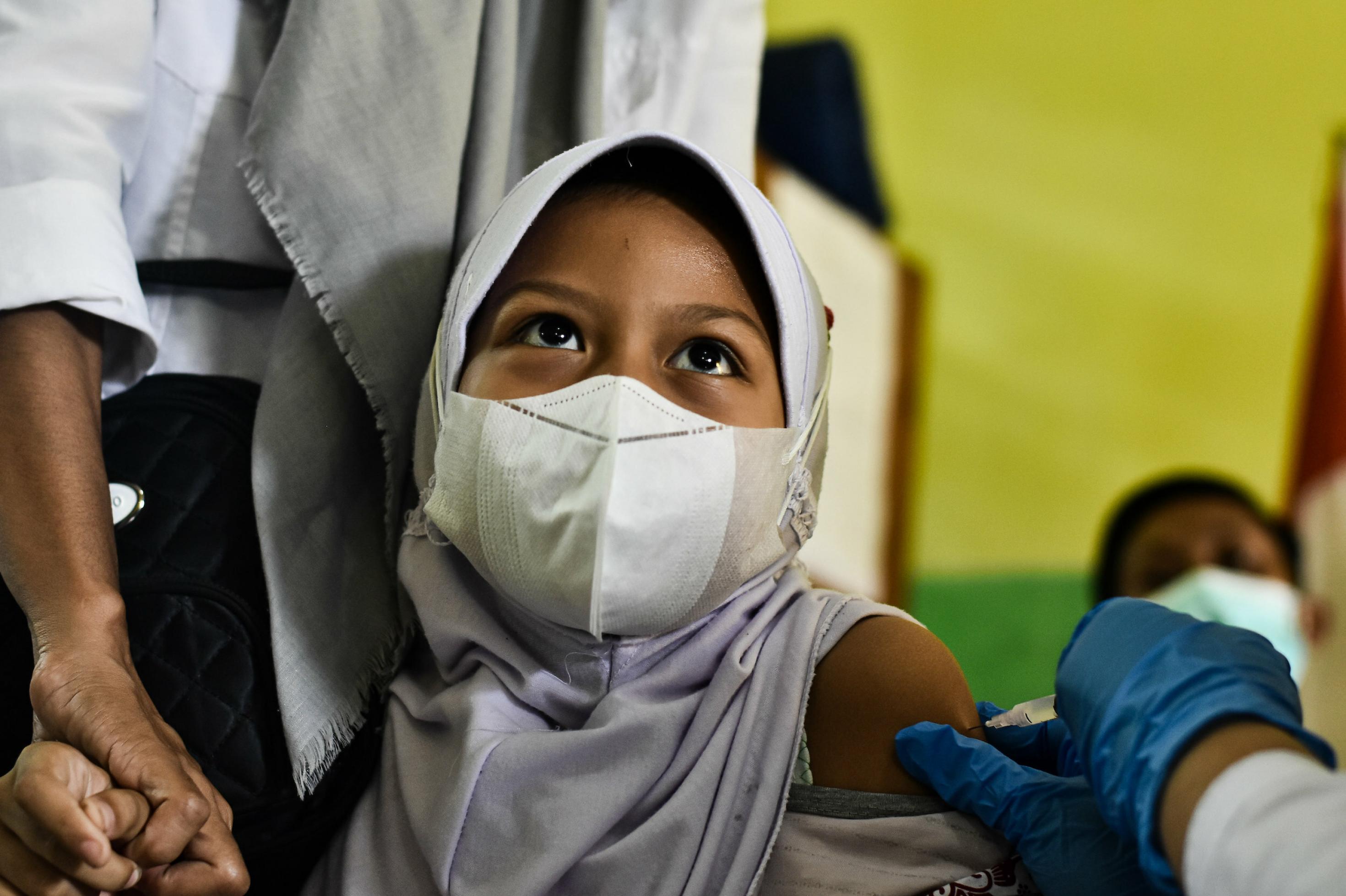 Ein Mädchen mit Kopftuch und Gesichtsmaske bekommt eine Impfung.