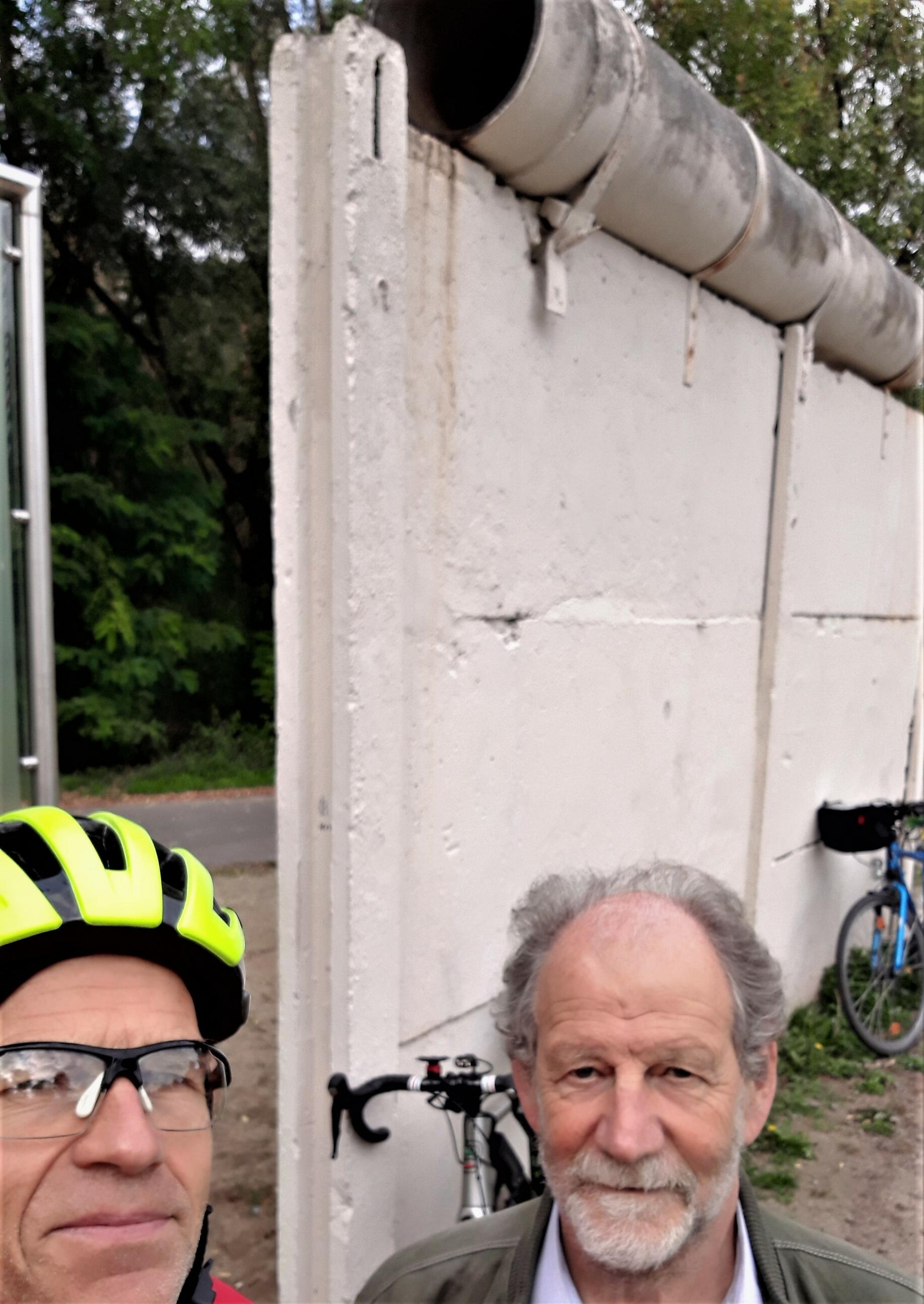 Roos und Cramer (rechts) im Selfie, im Hintergrund ist der original Mauerrest mit den daran gelehnten Fahrrädern der beiden Interviewpartner zu sehen.