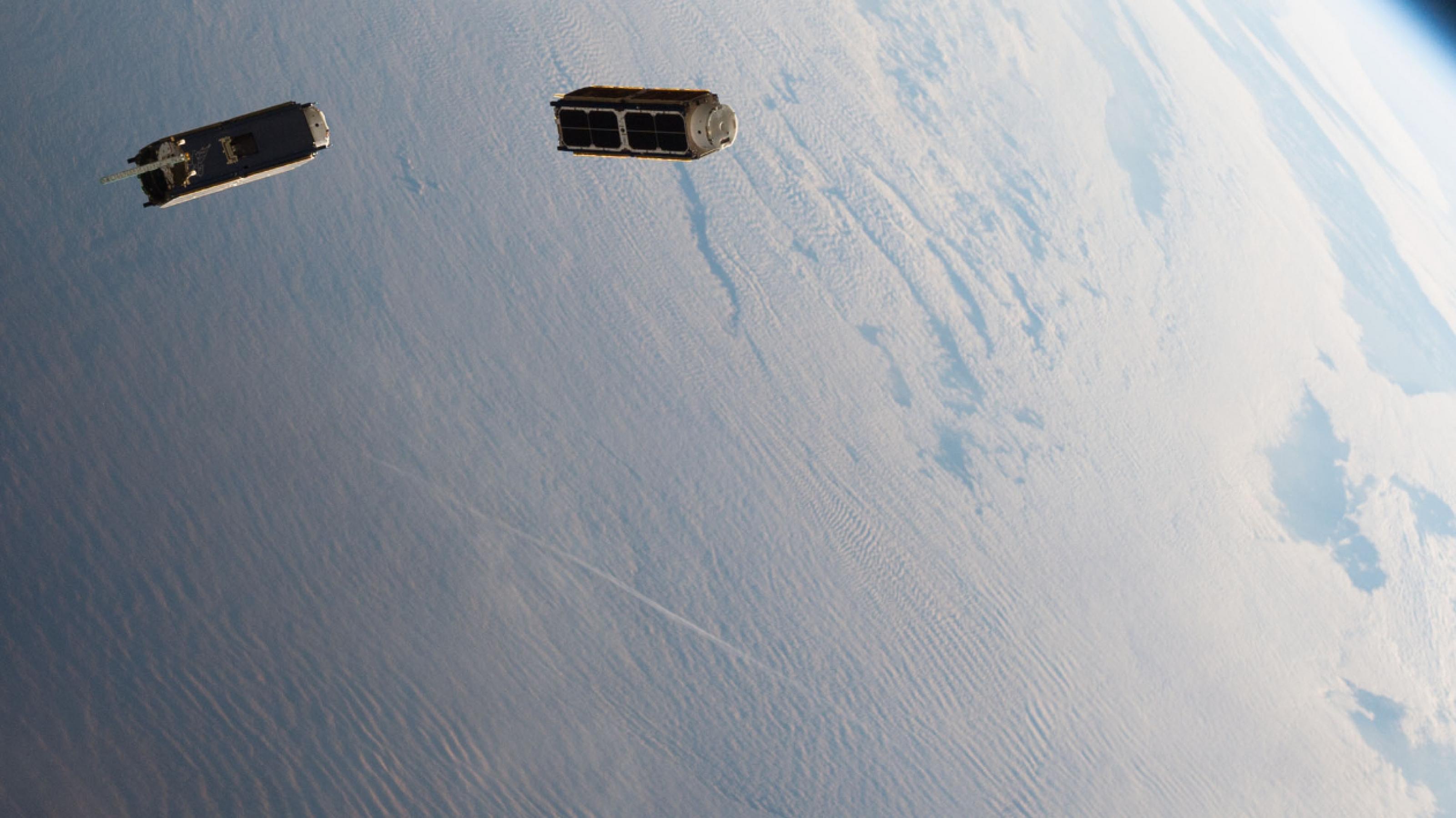 Zwei wie Schuhkartons geformte Satelliten driften um die blaue Erde