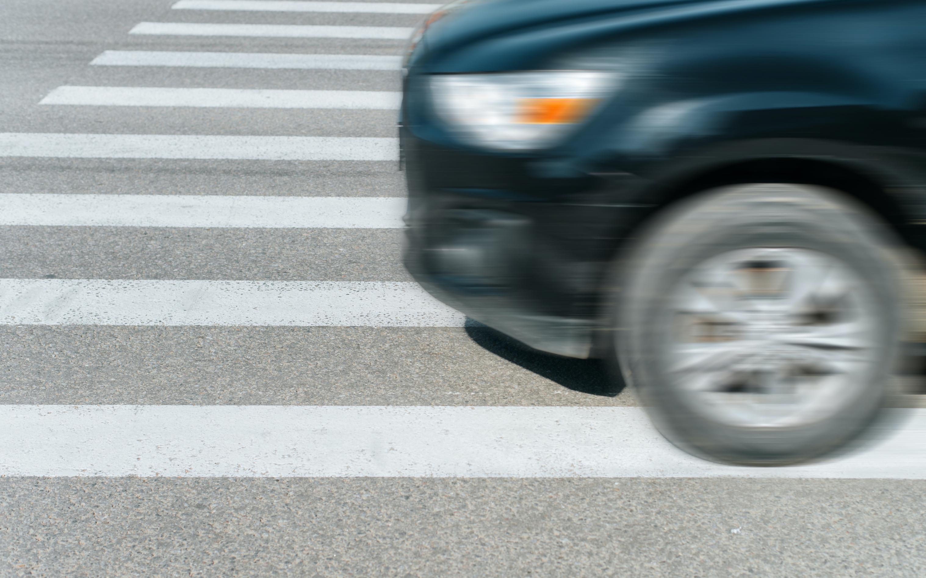 Ein schwarzes verschwommenes Auto fährt schnell auf einem Zebrastreifen