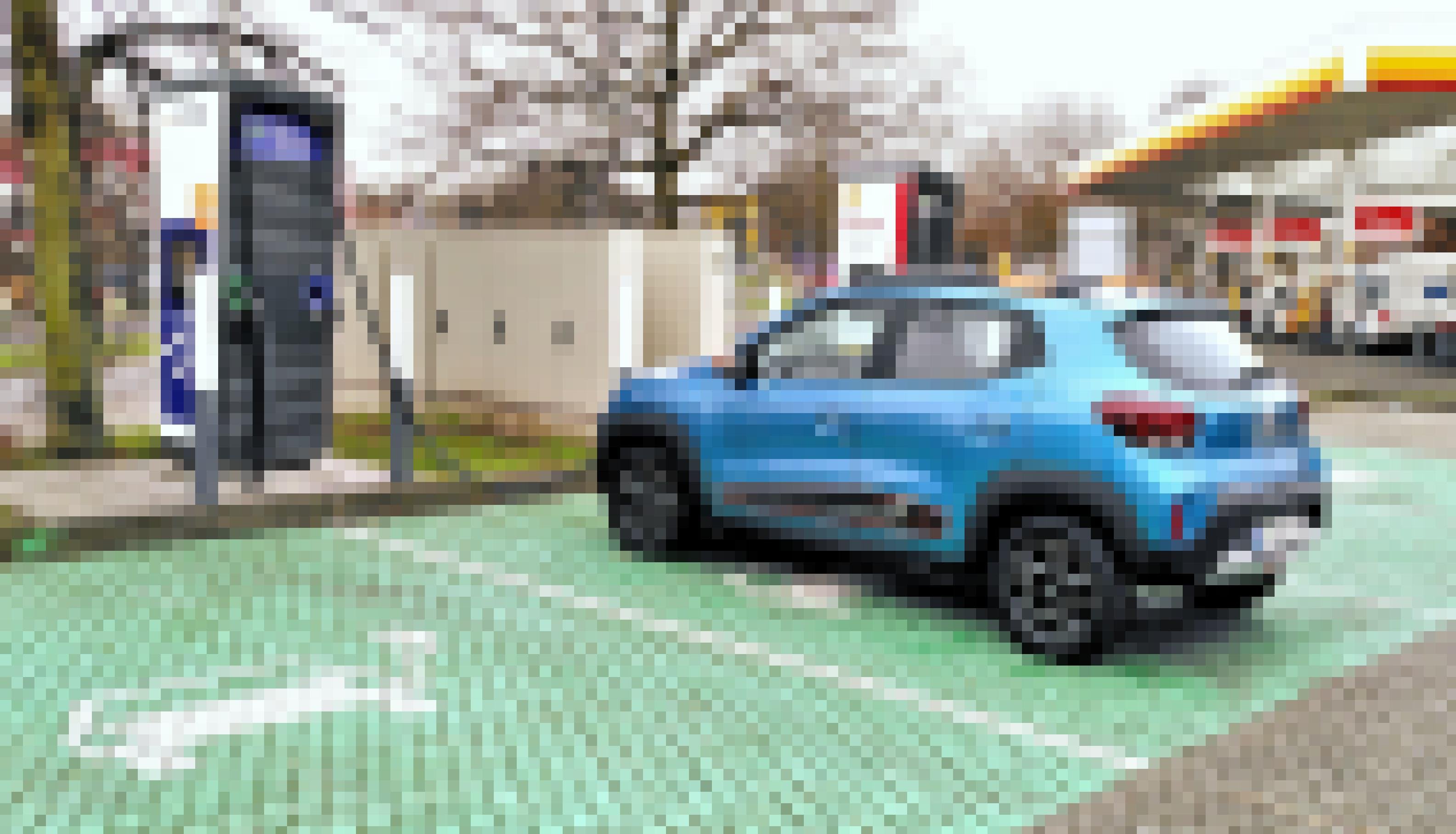 Ein Elektroauto ist an eine Ladestation angeschlossen. Im Hintergrund sieht man eine Tankstelle.