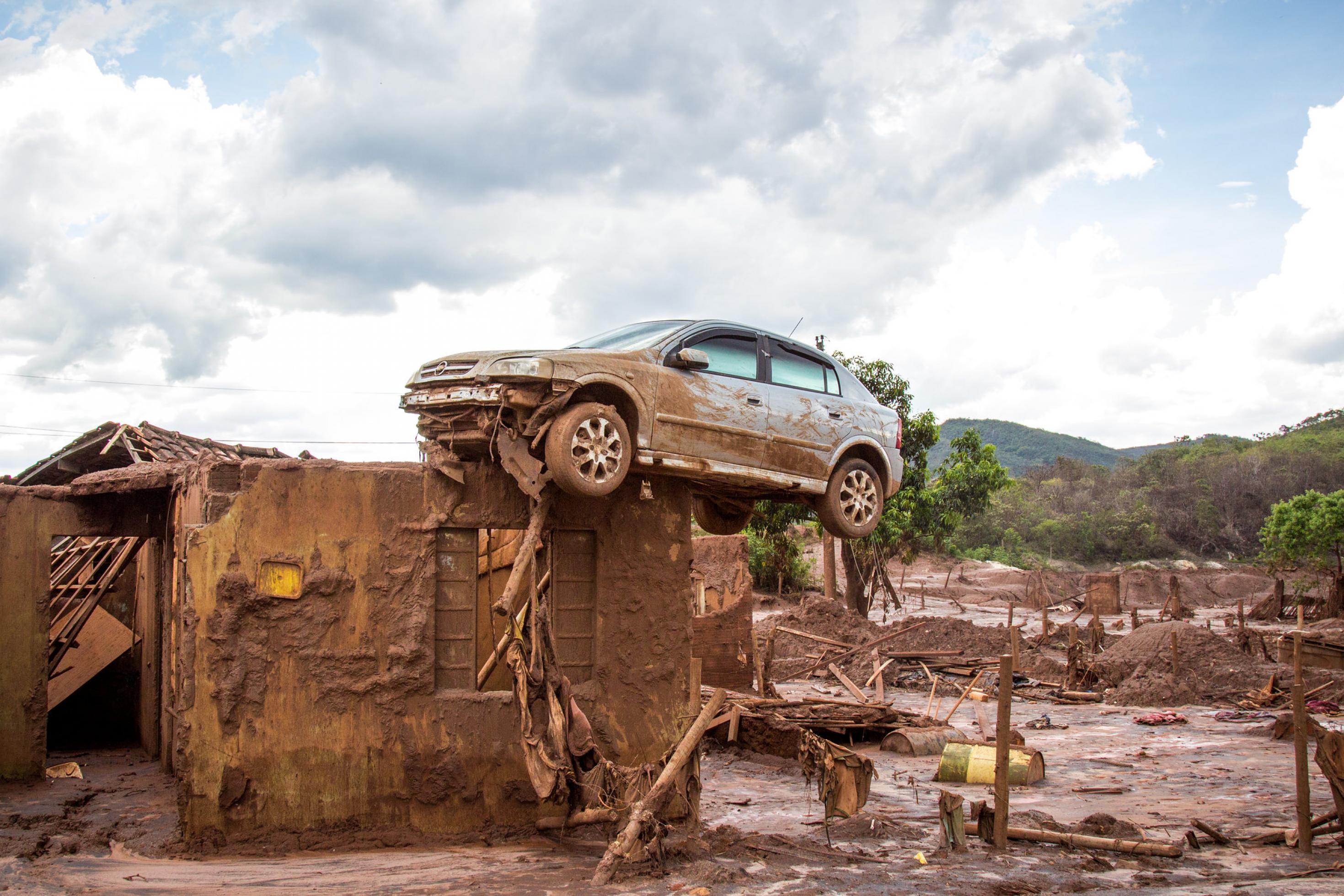 Eine Aufnahme von Bento Rodrigues zeigt kaputte, schlammüberströmte Reste von Häusern. Ein Auto ist vom Schlamm auf eine Mauer gehoben.
