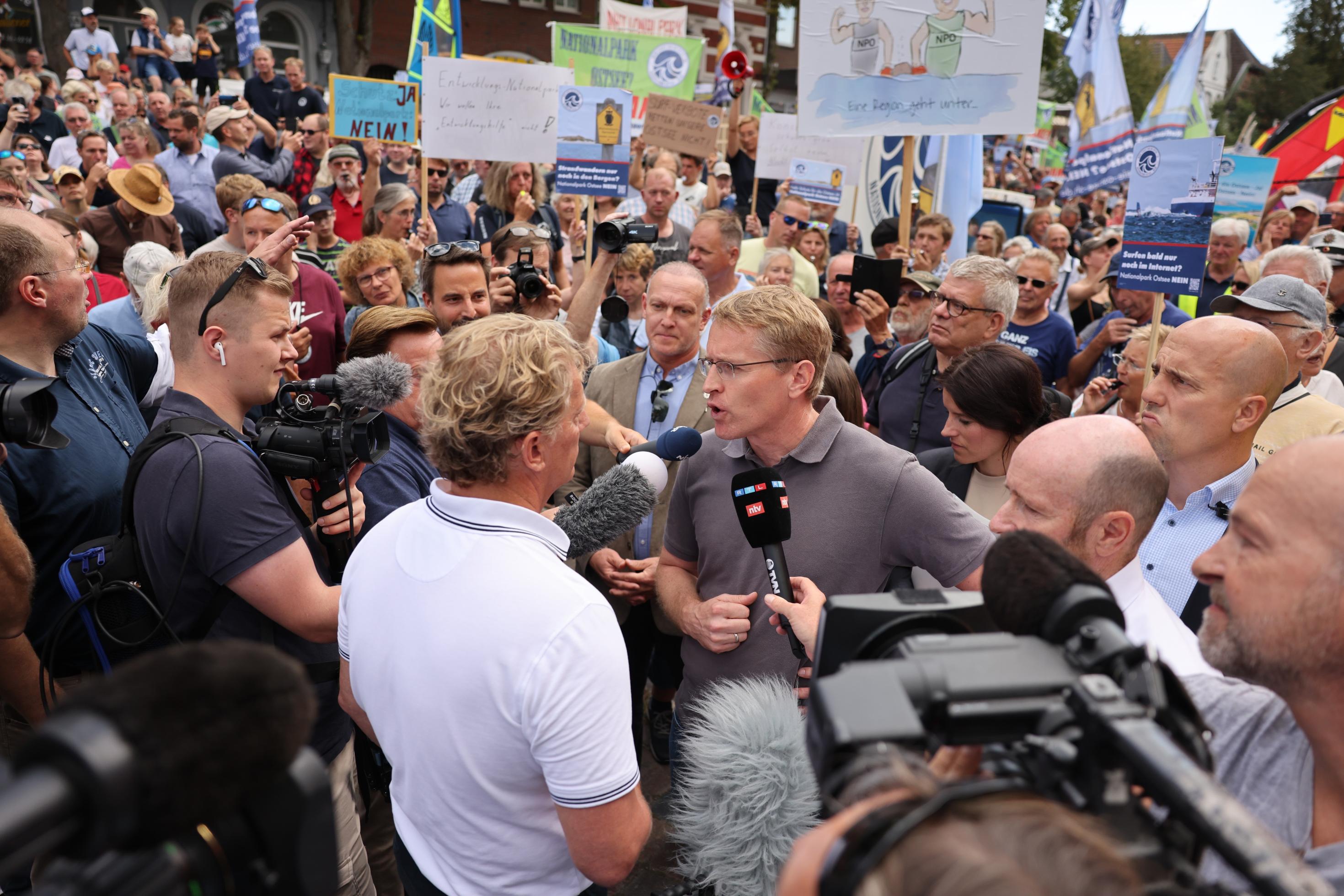 August 2023: Daniel Günther steht in einer mit Schildern protestierenden Menschenmenge und spricht in viele Mikrofone