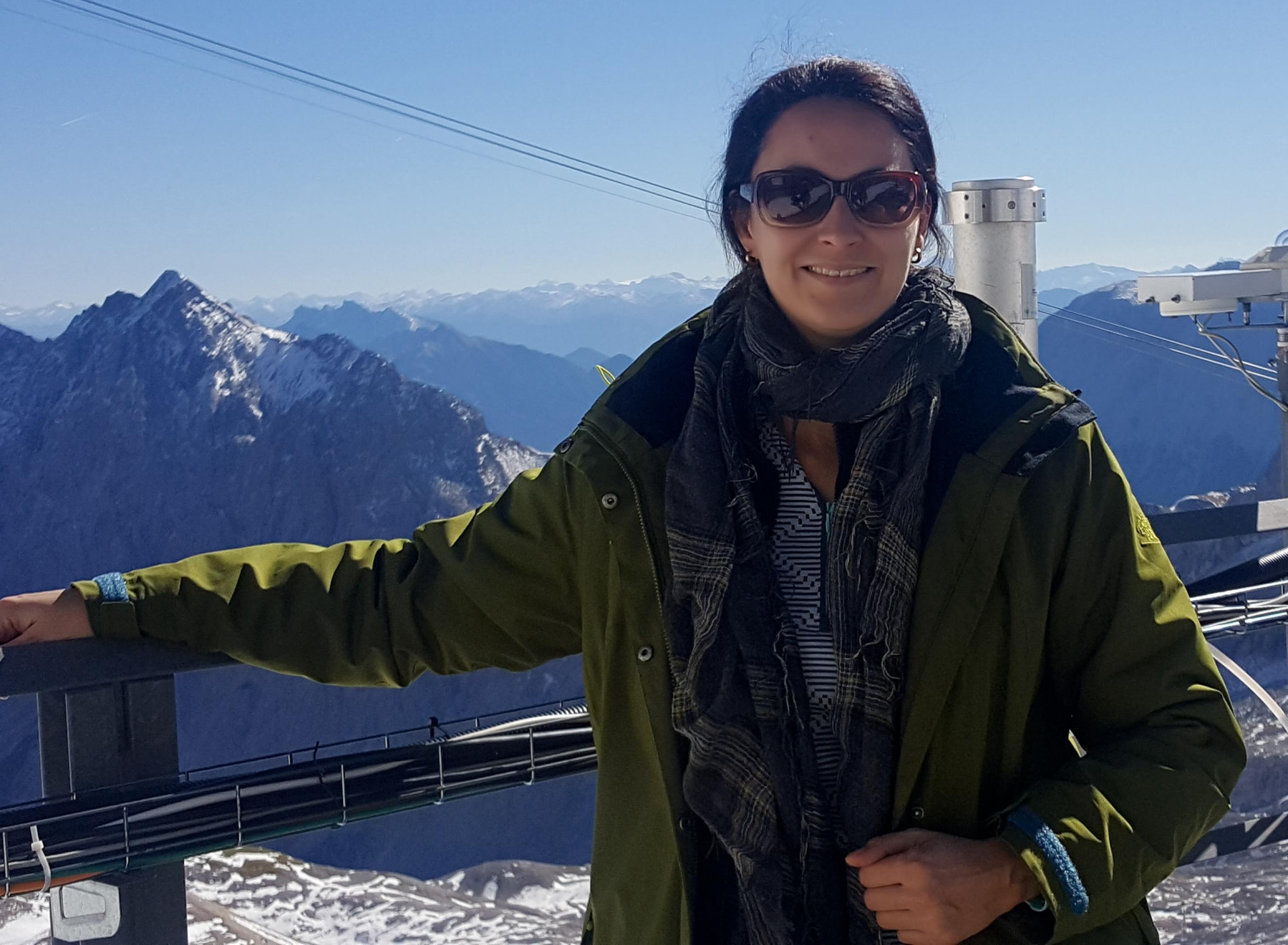 Klimasocial Autorin Daniela Becker steht auf dem Balkon der Forschungstation Schneefernerhaus auf der Zugspitze. Im Hintergund sind Berge zu sehen.