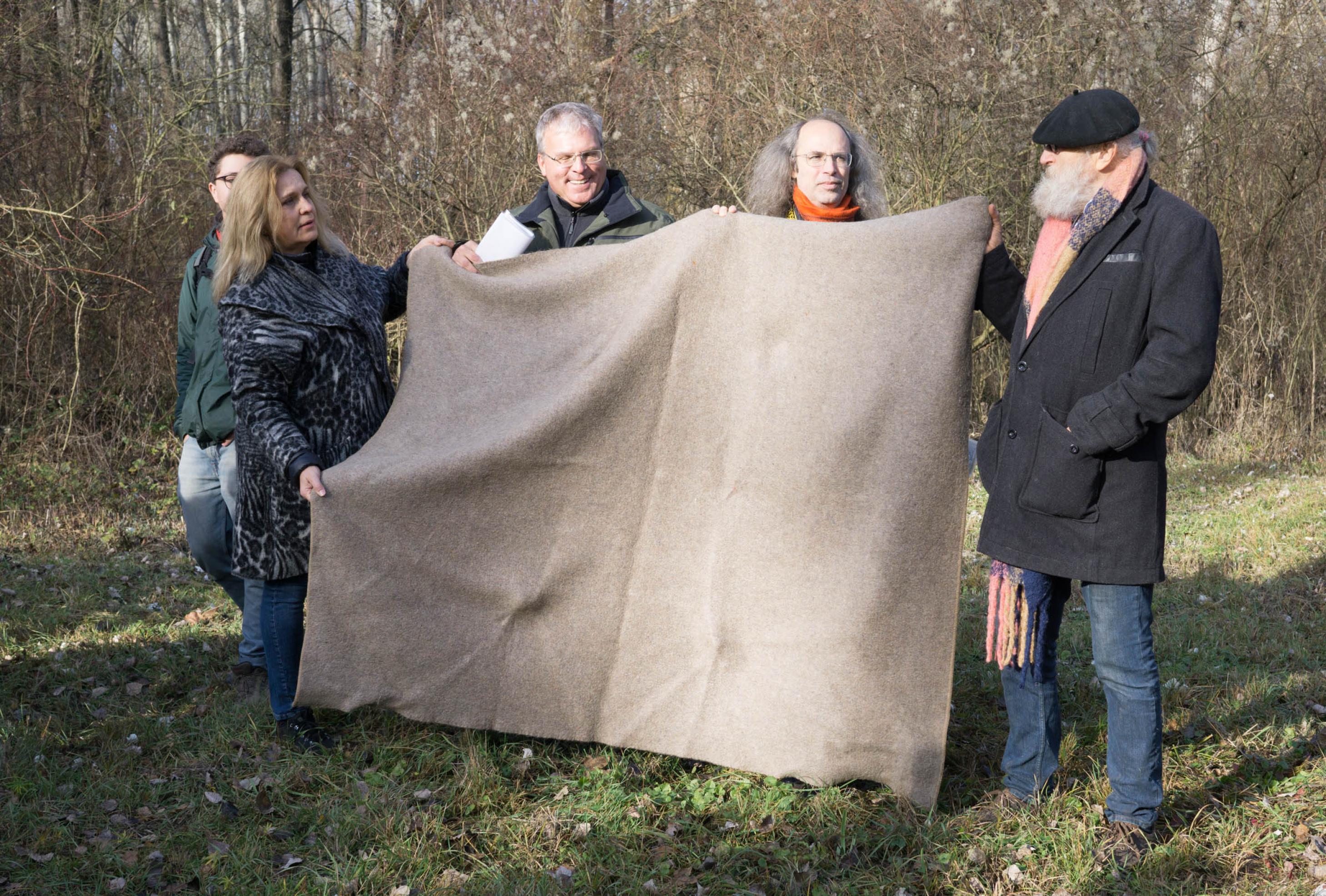 Menschen auf einer Waldlichtung halten eine Wolldecke hoch.