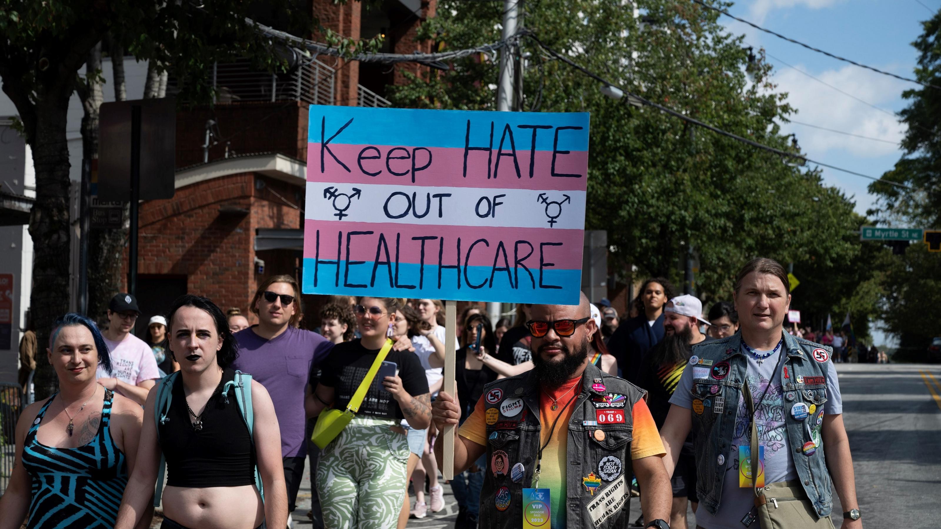 Eine Gruppe von Menschen auf einer Demonstration. Einer trägt ein Schild mit folgendem Text: „Keep health out of healthcare.“