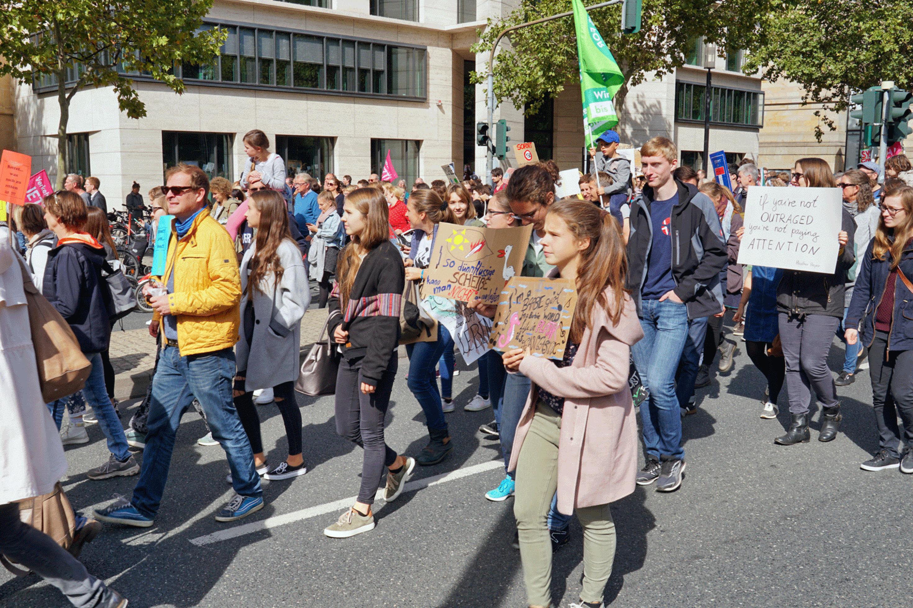 Eine große Gruppe Jugendlicher demonstriet, geht mit Slogans auf Pappschildern und Fahnen auf der Straße einer stadt.