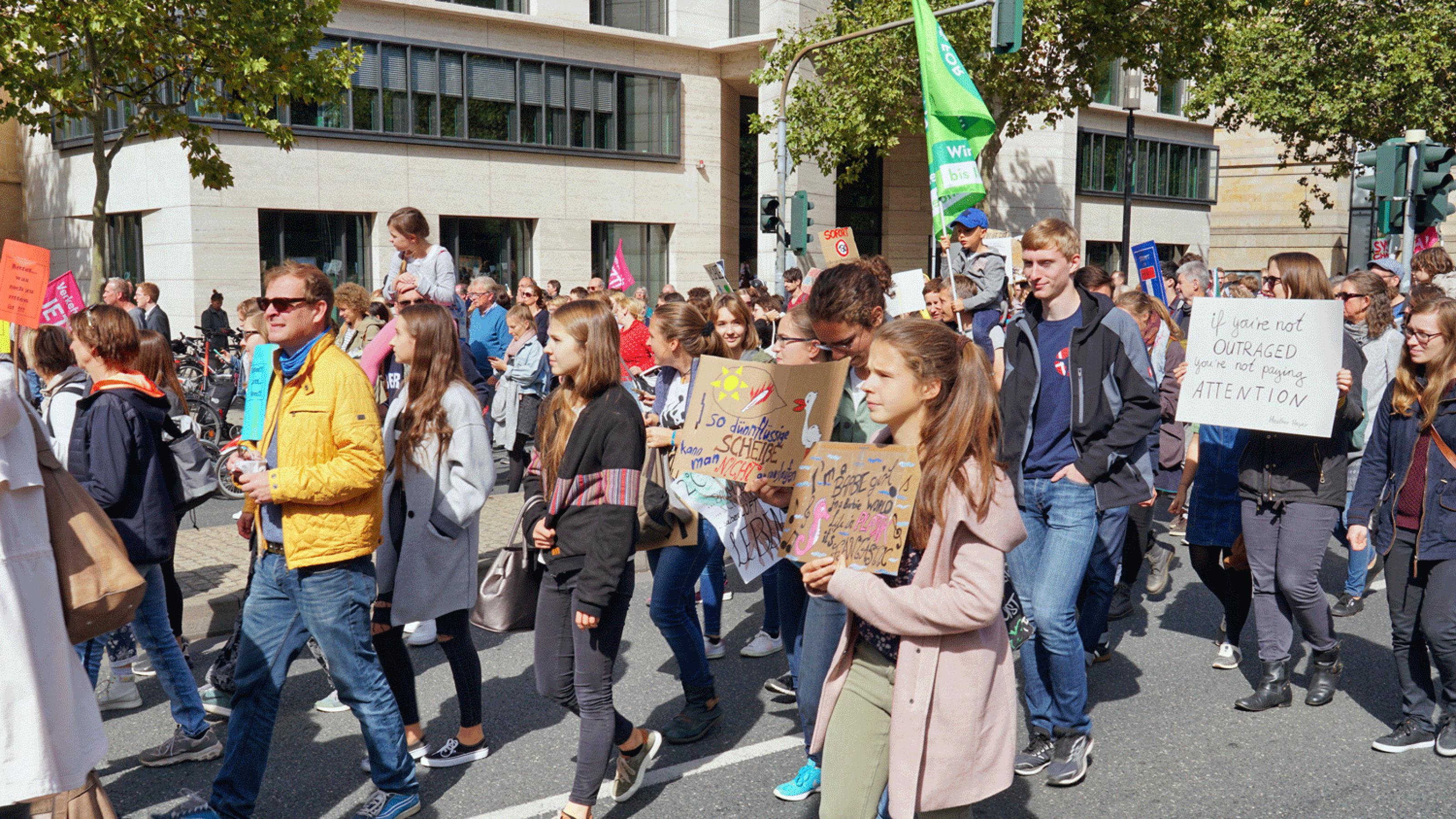 Eine große Gruppe Jugendlicher demonstriet, geht mit Slogans auf Pappschildern und Fahnen auf der Straße einer stadt.