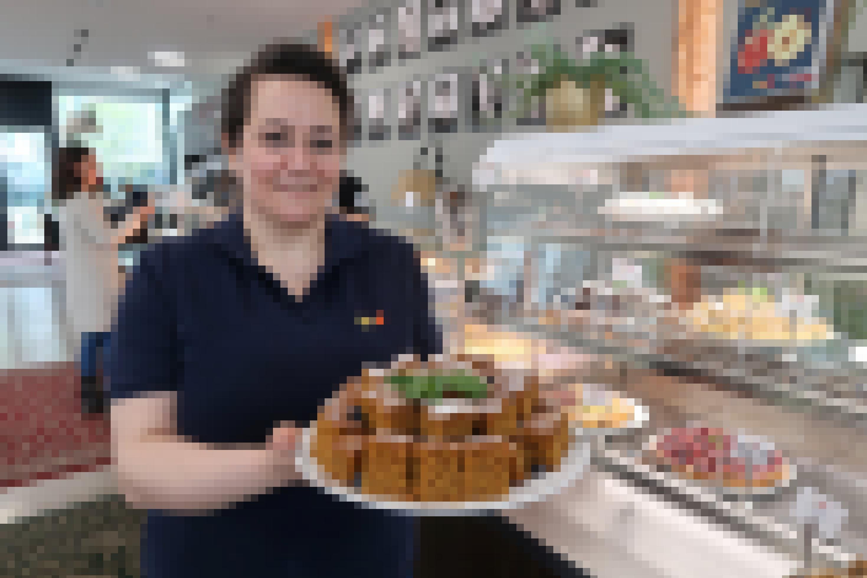 Frau steht vor Kuchen-Theke mit Gebäck-Teller in der Hand