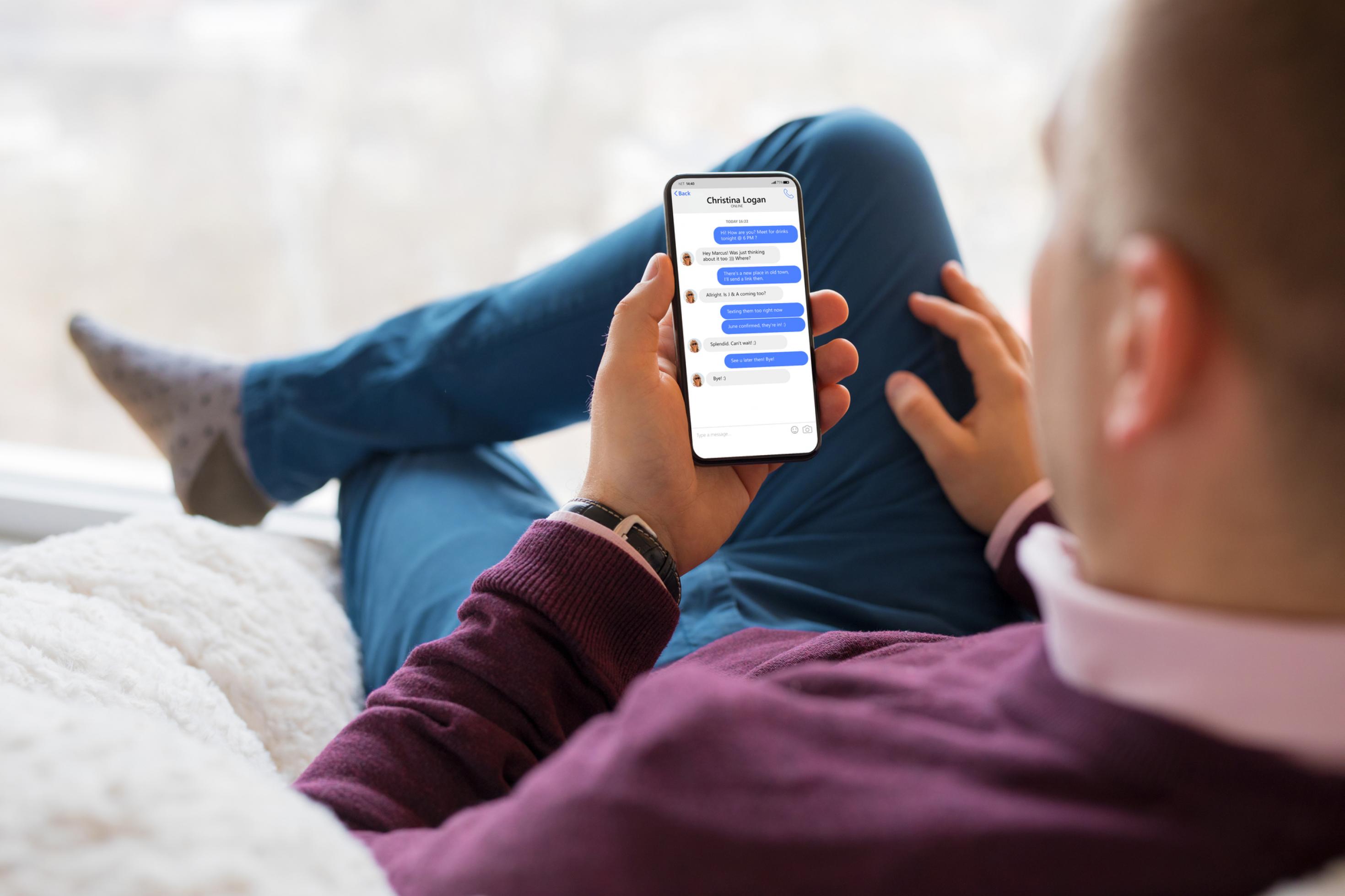 Ein mittelalter Mann sitzt auf dem Sofa und nutzt am Smartphone einen Messenger-Dienst.