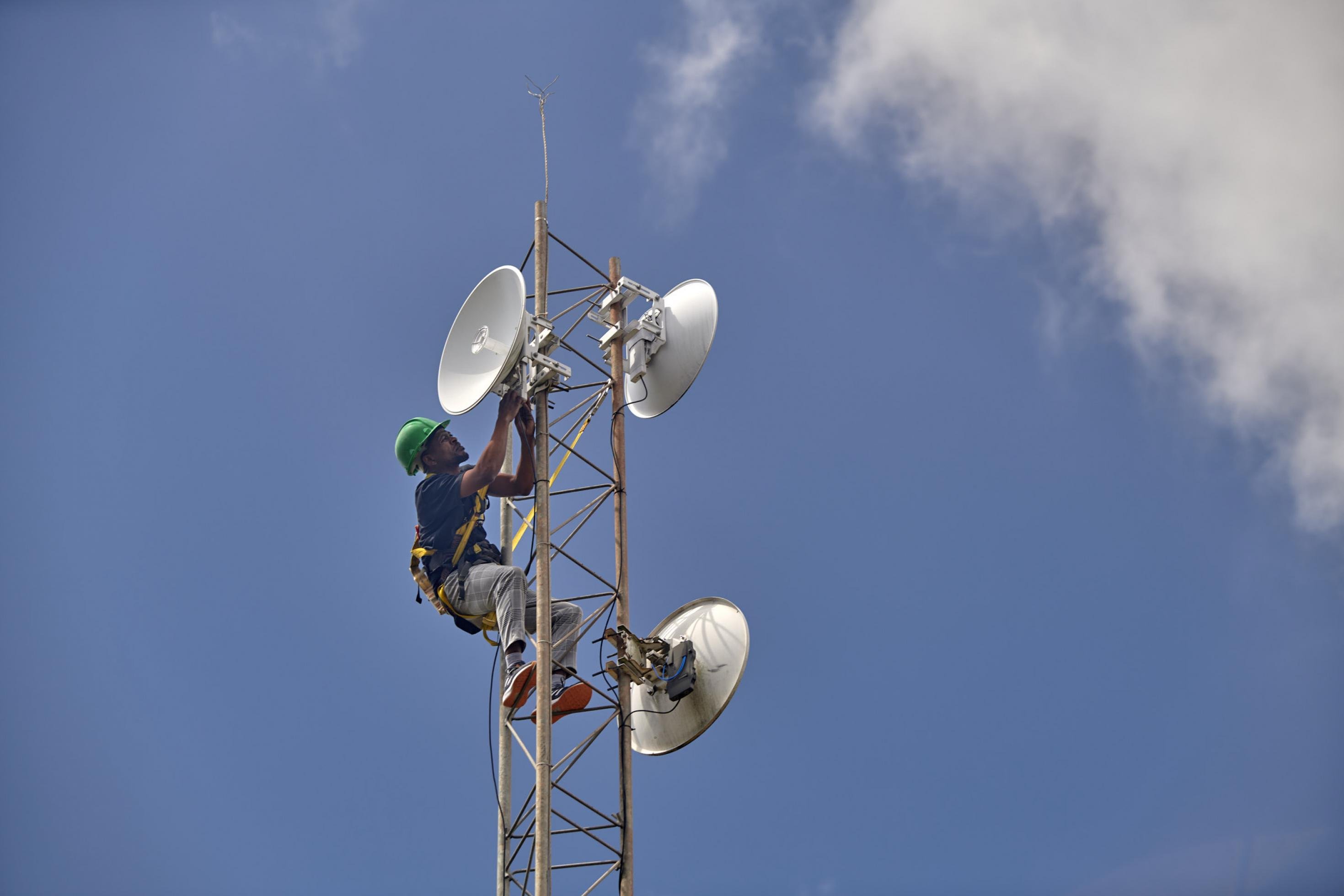 Auf dem Bild ist ein Techniker mit Helm zu sehen, der ganz oben auf einen Mast geklettert ist, der zum kommunalen Netzwerk in Mankosi gehört.