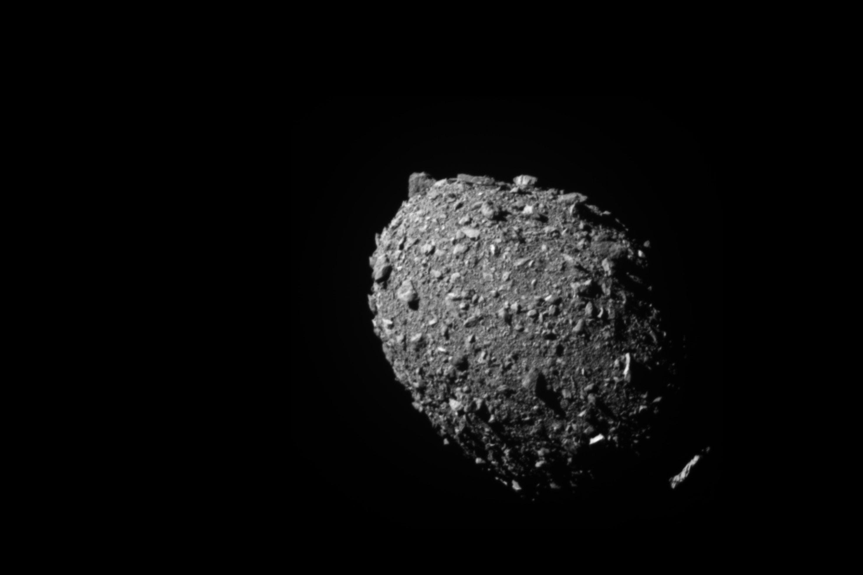 Ein eiförmiger grauer Asteroid, der von großen Brocken übersät ist und so sehr pockennarbig wirkt.