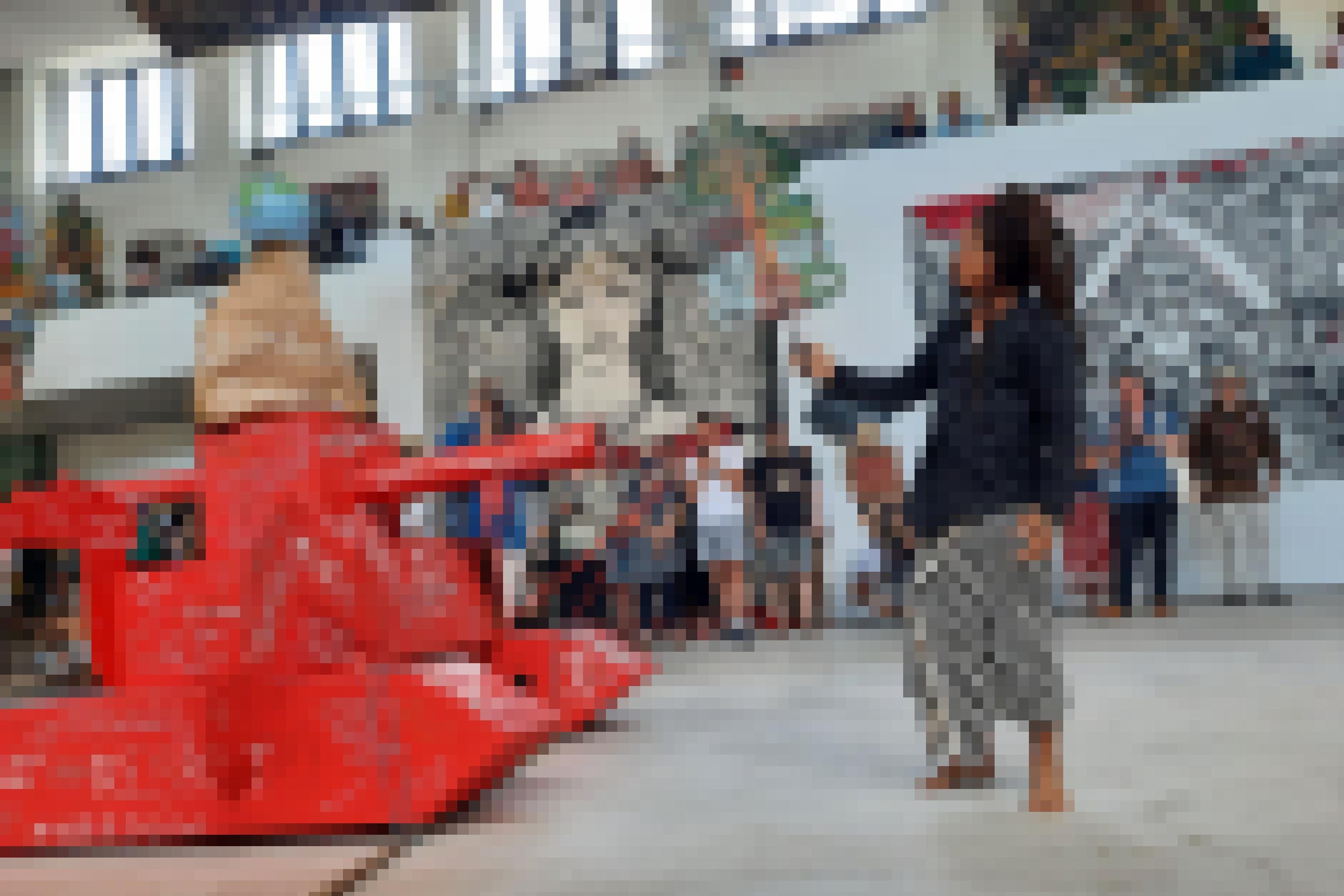 Ein Mitglied von Taring Padi steht mit einer Wayang-Figur in der Hand vor einem Pappmaché-Gefährt, das halb Panzer, halb Bagger darstellt.
