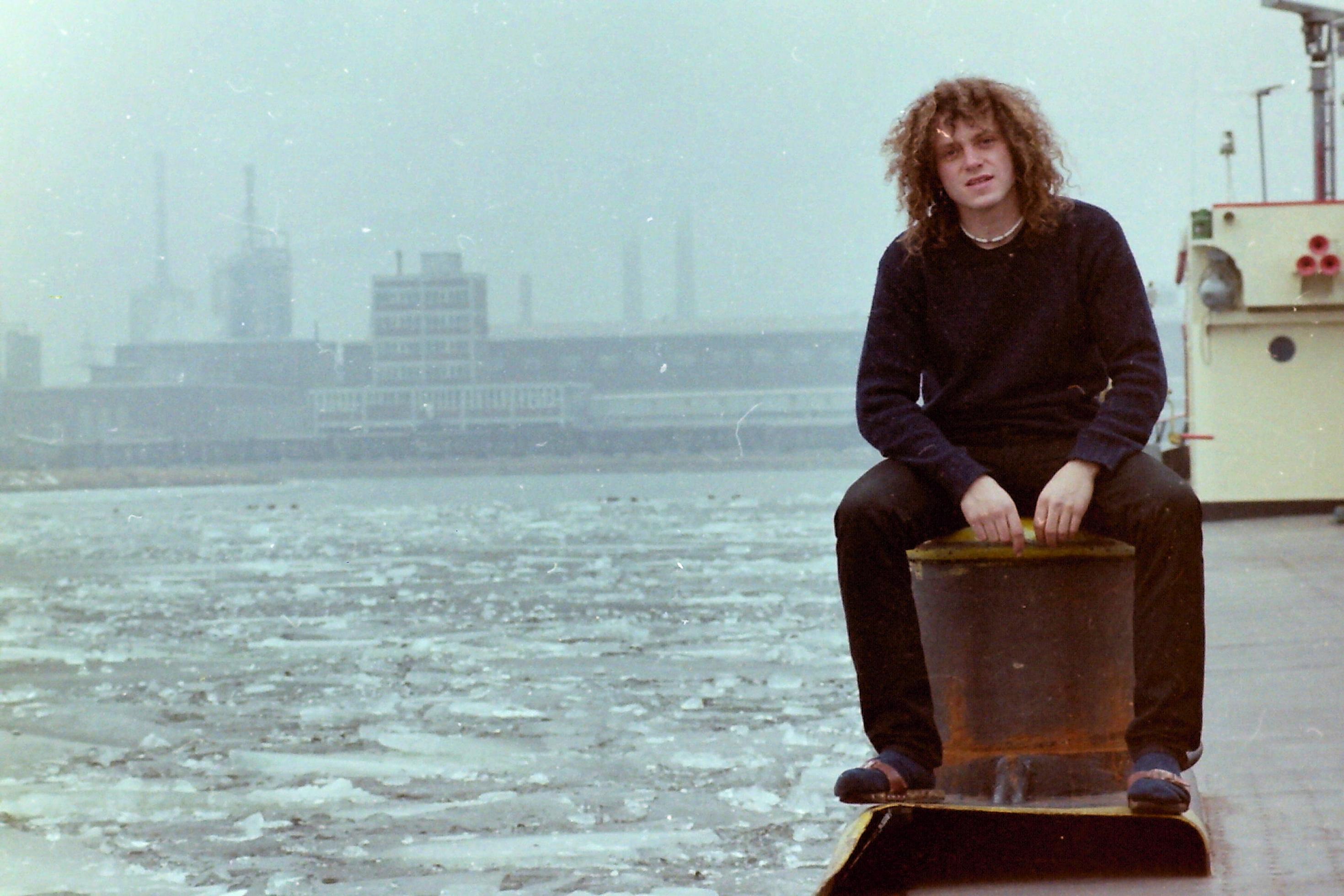 Junger Mann mit langen lockigen Haaren am Hafen